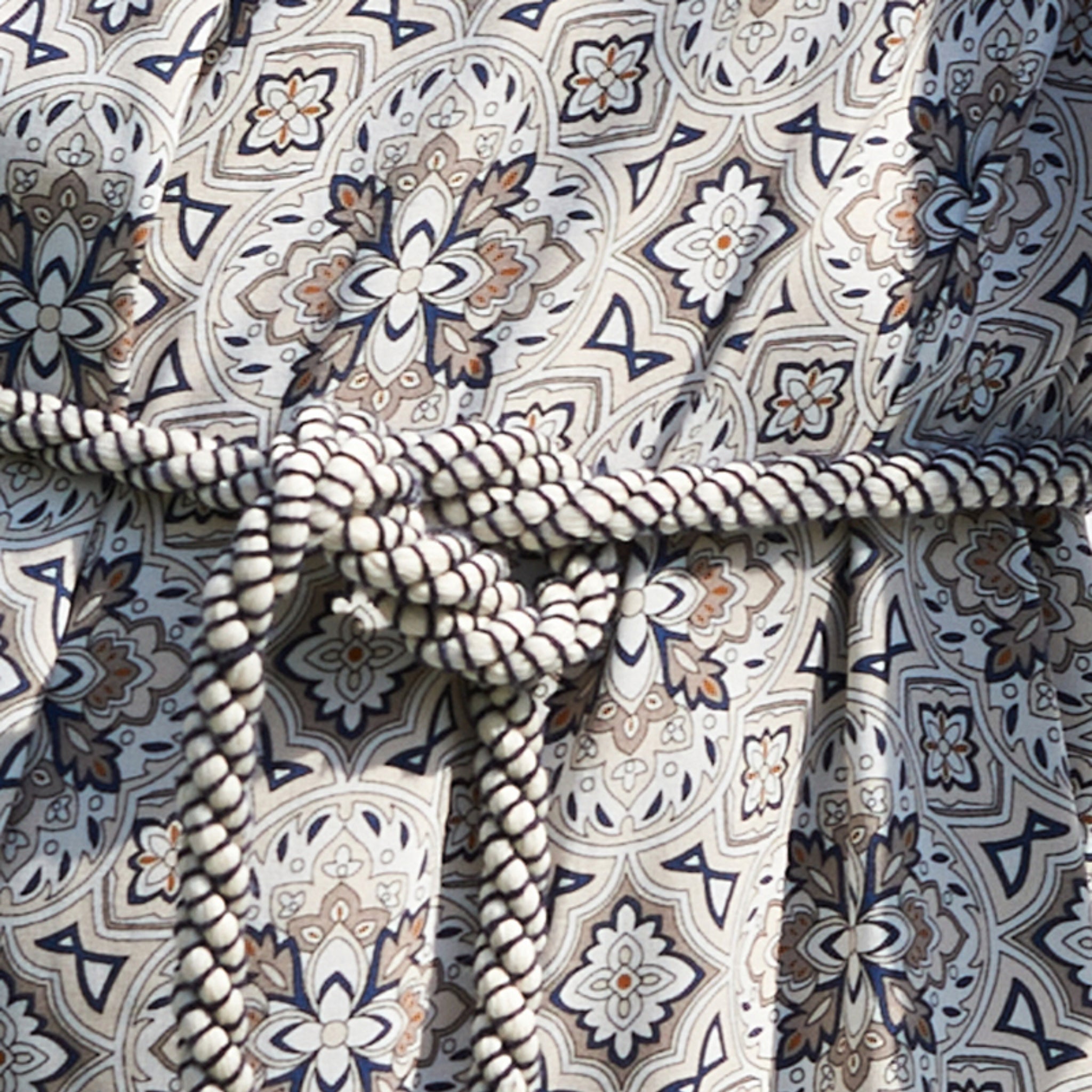 Nahaufnahme eines Stoffes mit einem detaillierten, floralen Muster in Blau, Braun und Weiß, gehalten von einem geflochtenen Seil.