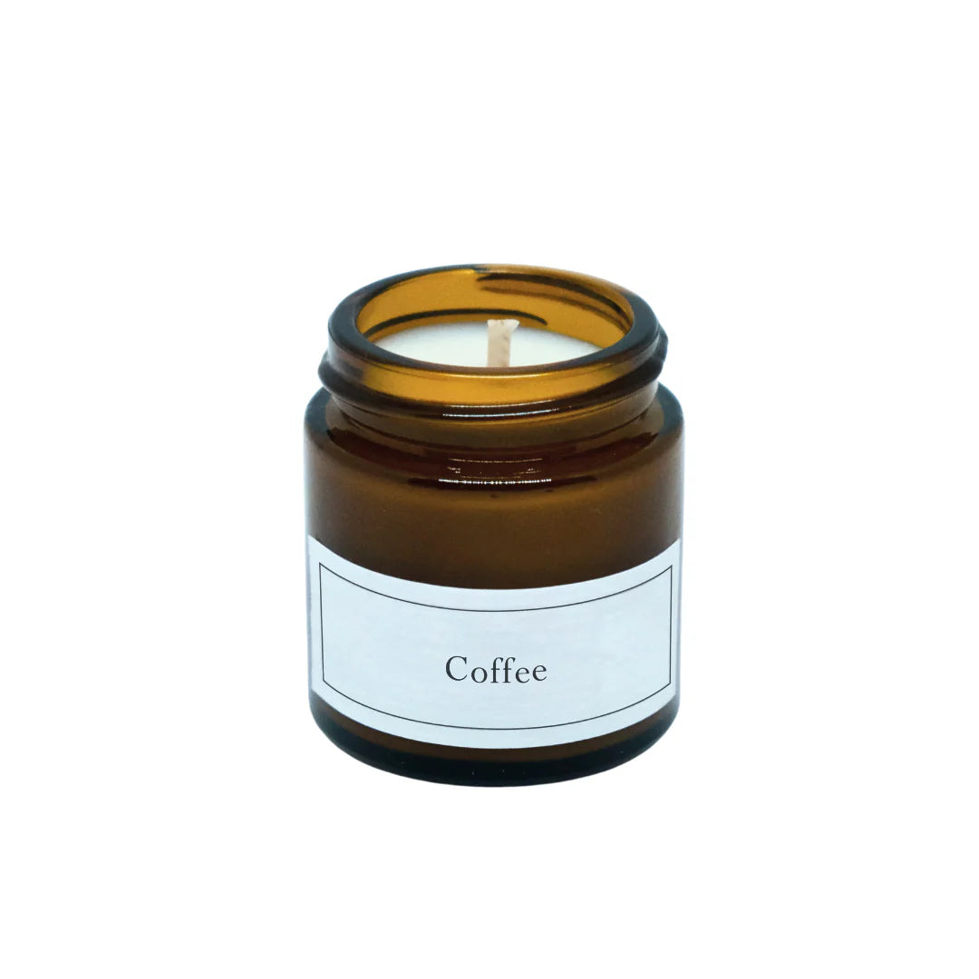 Eine braune Glaskerze mit einem weißen Etikett mit der Aufschrift Coffee. Die Kerze ist unbenutzt, mit einem zentrierten Docht und ohne Deckel vorhanden.