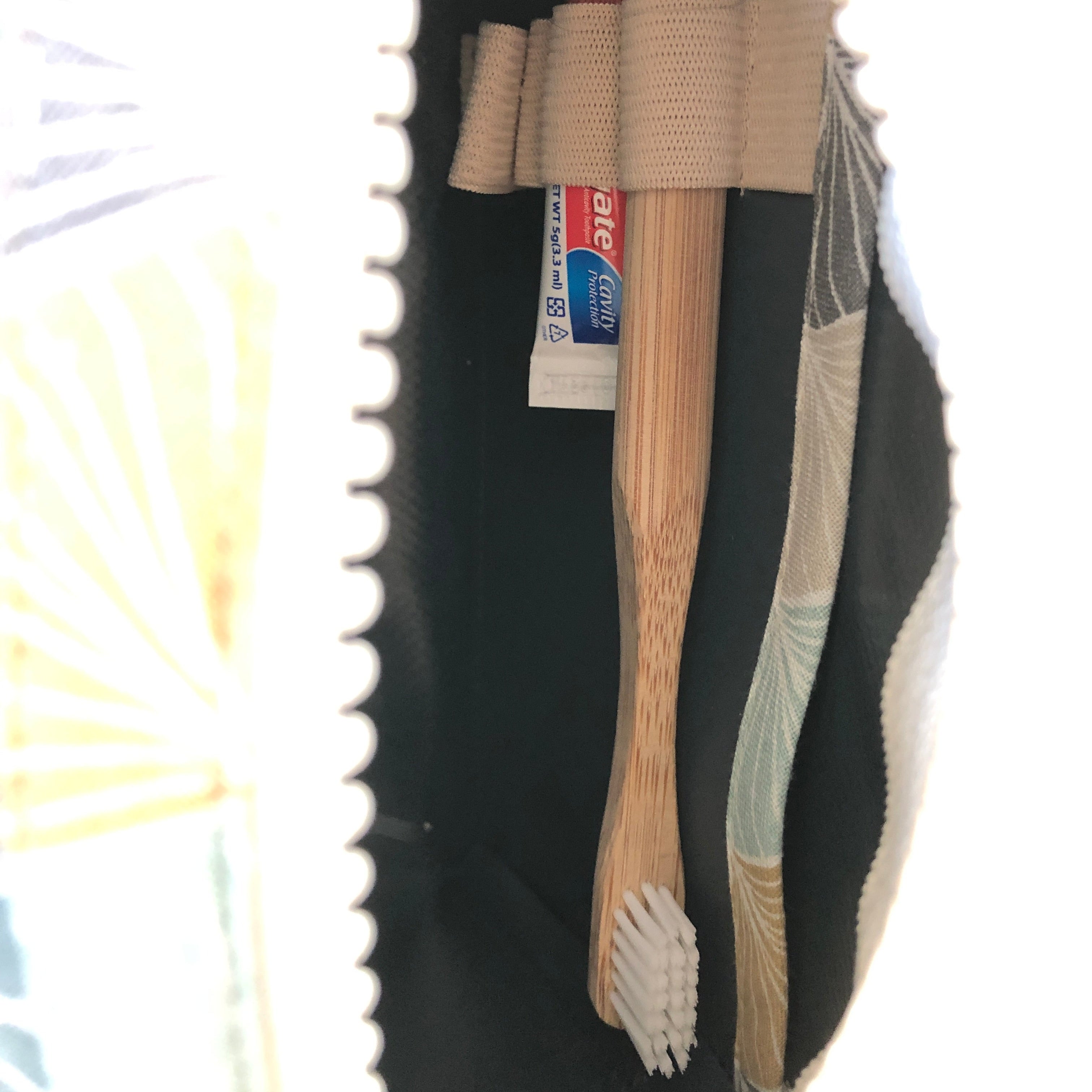 Zahnbürste aus Holz und Zahnpastatube in einer geöffneten Kulturtasche mit buntem Stoffmuster im Inneren.