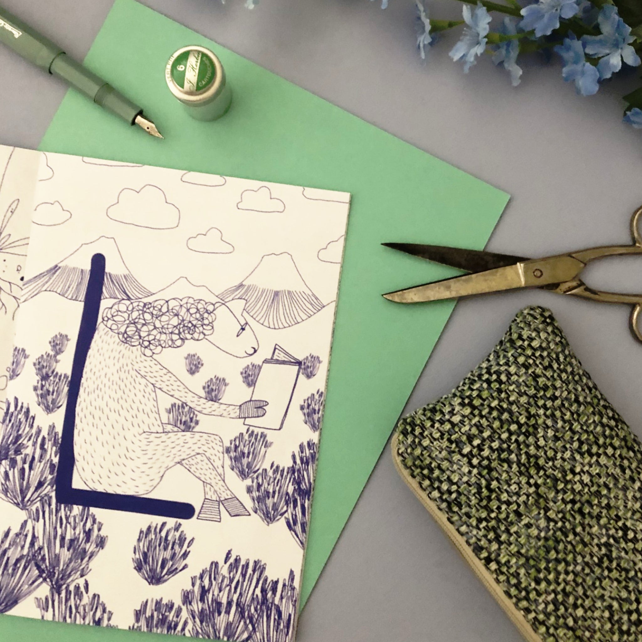 Zeichnung eines Lesenden in einer lila Landschaft, zusammen mit einer Schere, einem Stift und grünem Papier arrangiert.