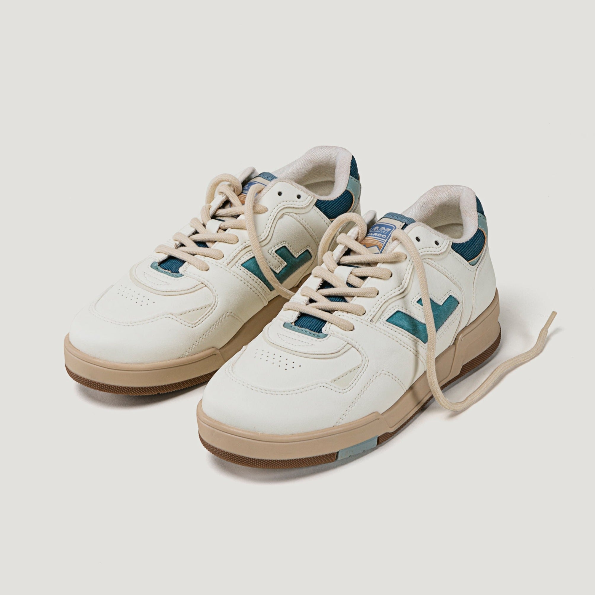 Weiße Sneakers mit brauner Sohle und blauen Details, die auf einem weißen Hintergrund stehen.