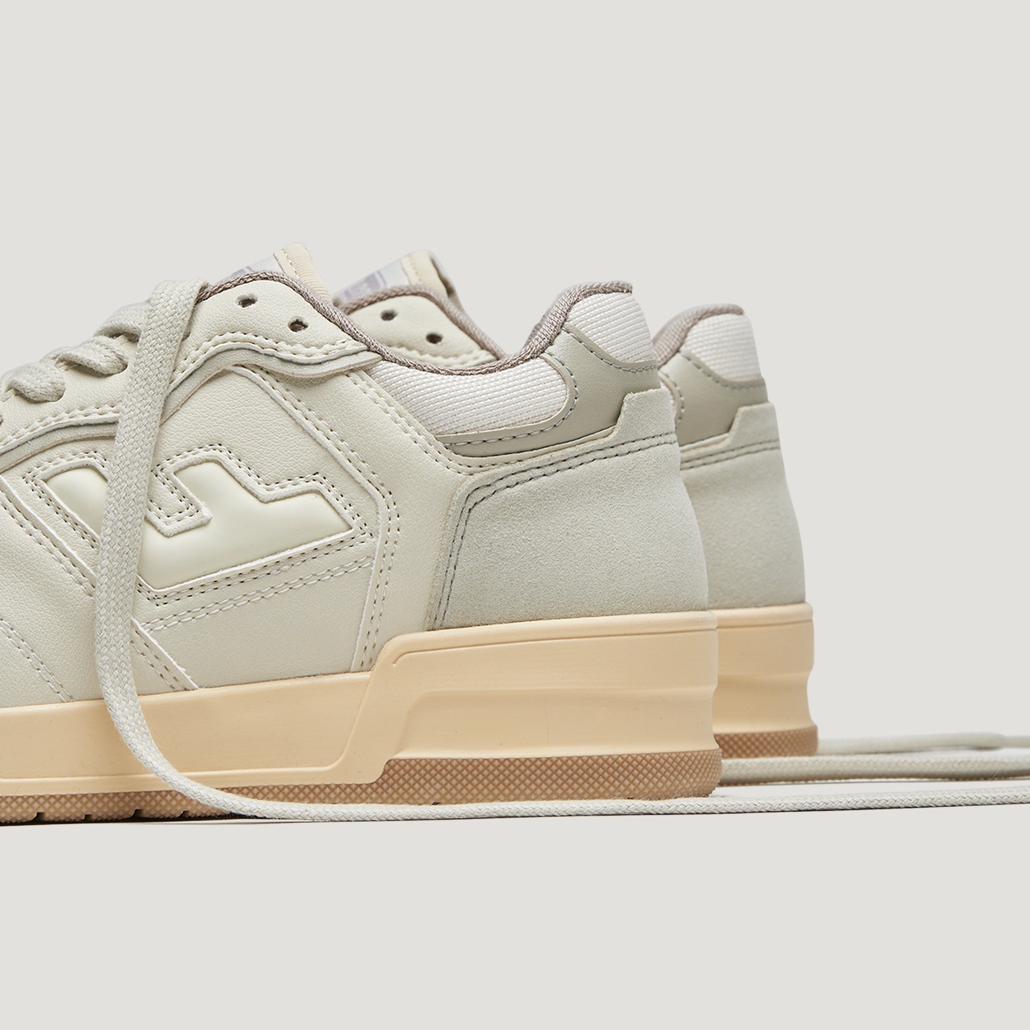 Beige Turnschuhe mit Schnürsenkeln und einer hellbraunen Sohle, von der Seite gezeigt.