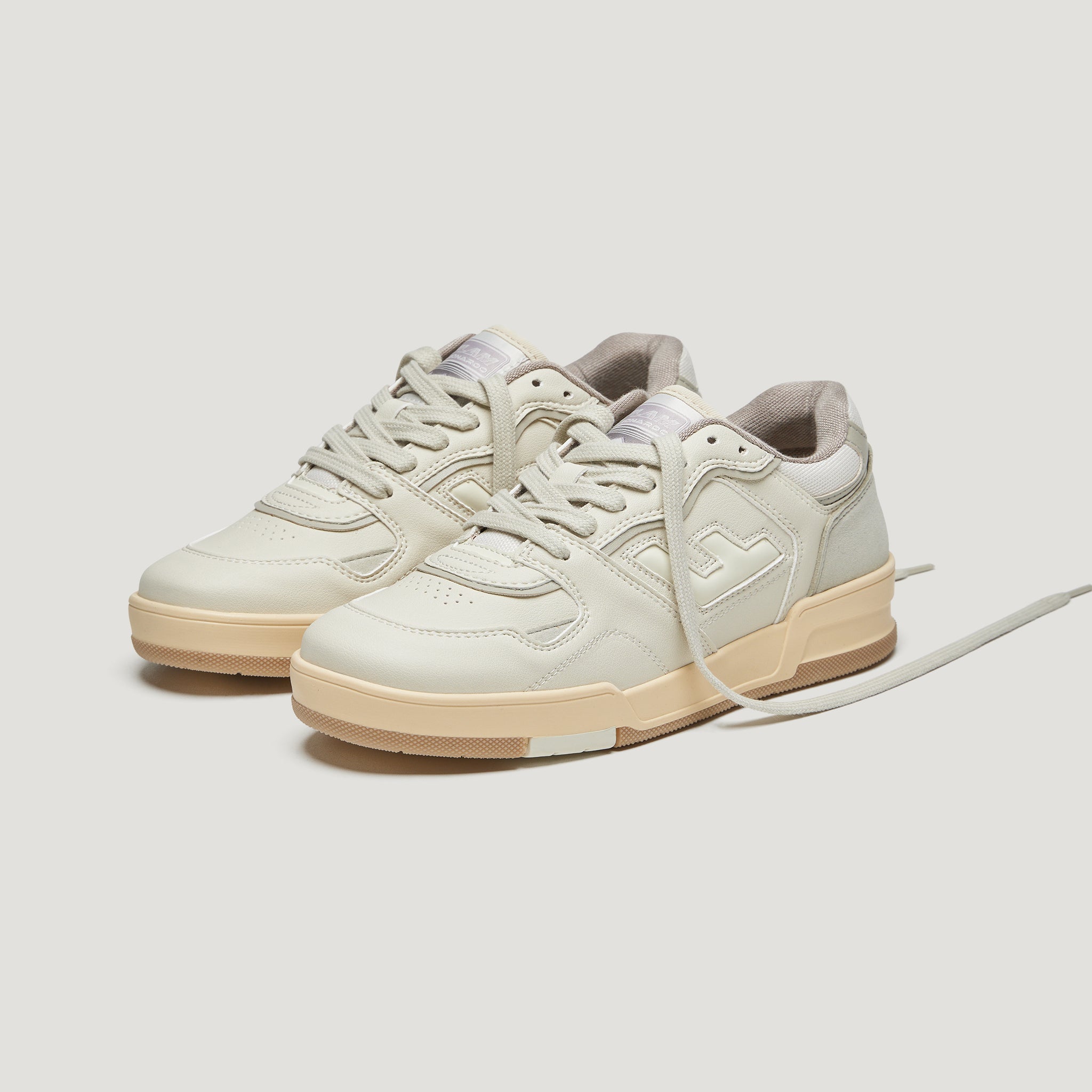 Beige Sneakers mit dicken Sohlen auf weißem Hintergrund, einer der Schnürsenkel ist gelöst.