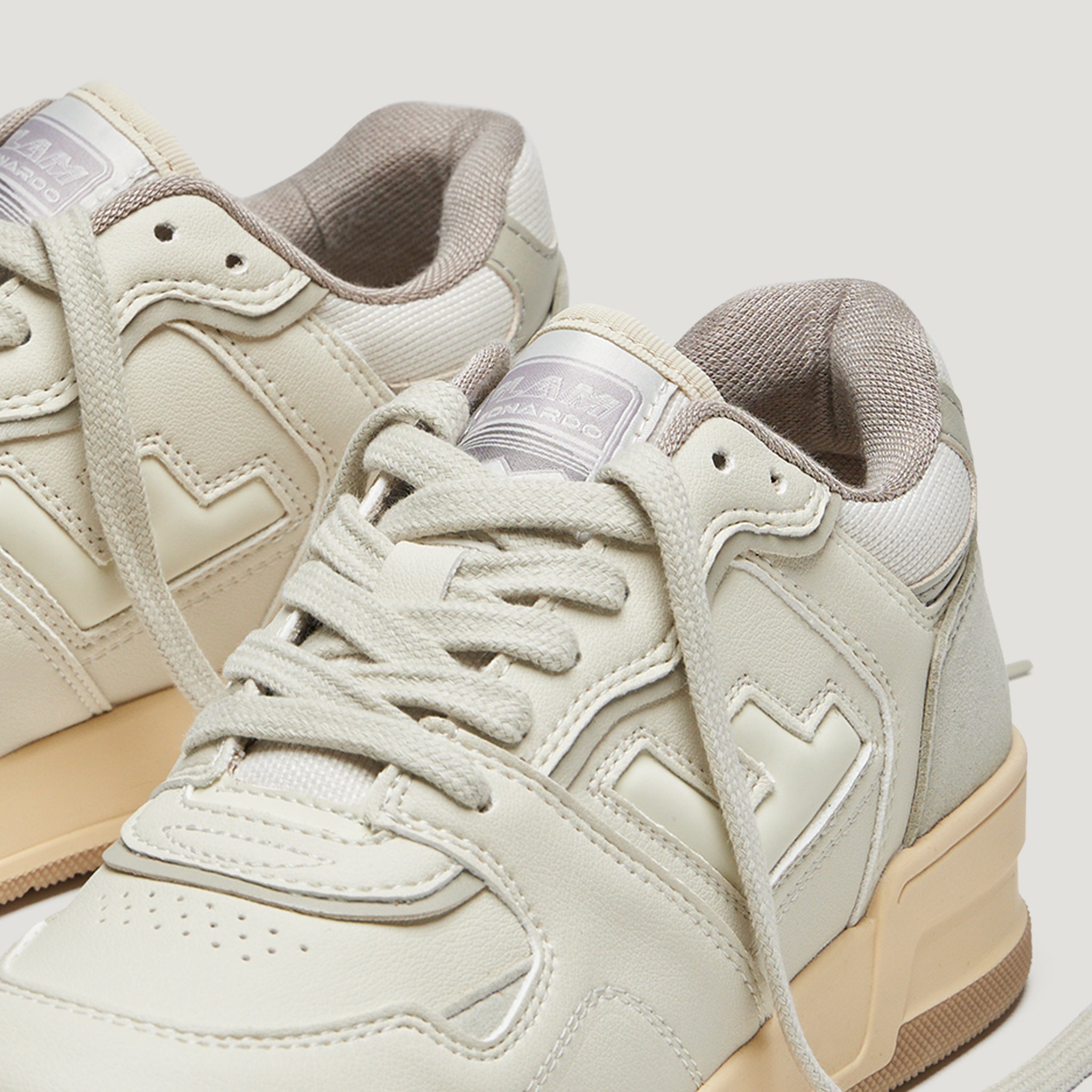 Beigefarbene Turnschuhe mit cremefarbenen Details und beigen Gummisohlen auf weißem Hintergrund.