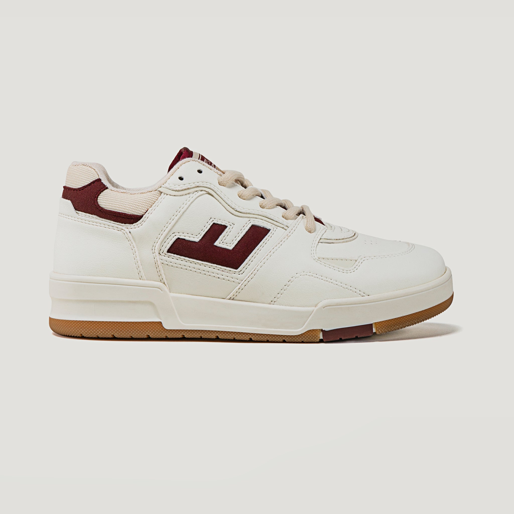 Weißer Sneaker mit braunen Akzenten und einer Gummisohle, seitlich ein stilisiertes "J"-Logo.