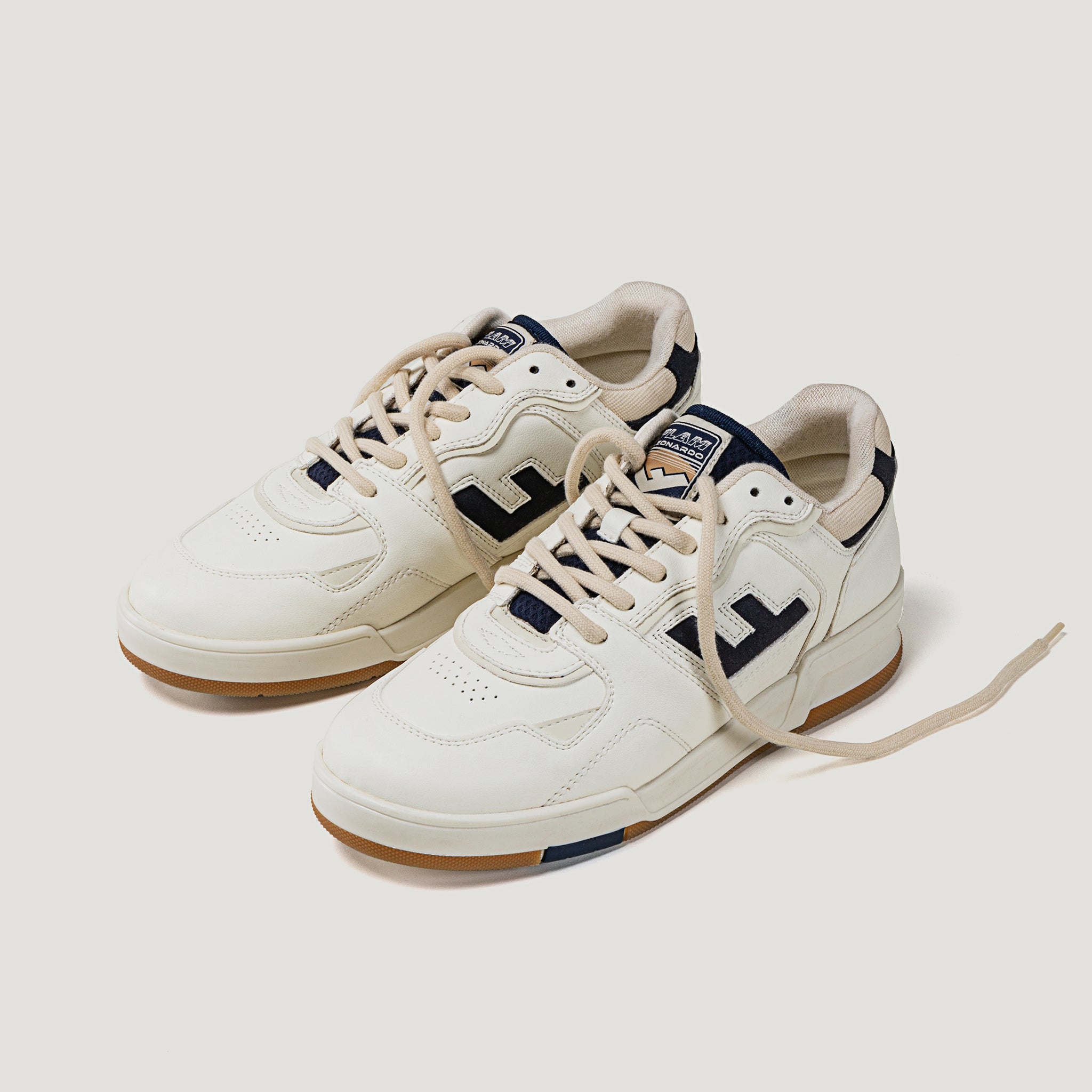 Weiße Sneaker mit dunklen Details und beigem Schnürsenkel, auf hellem Hintergrund.