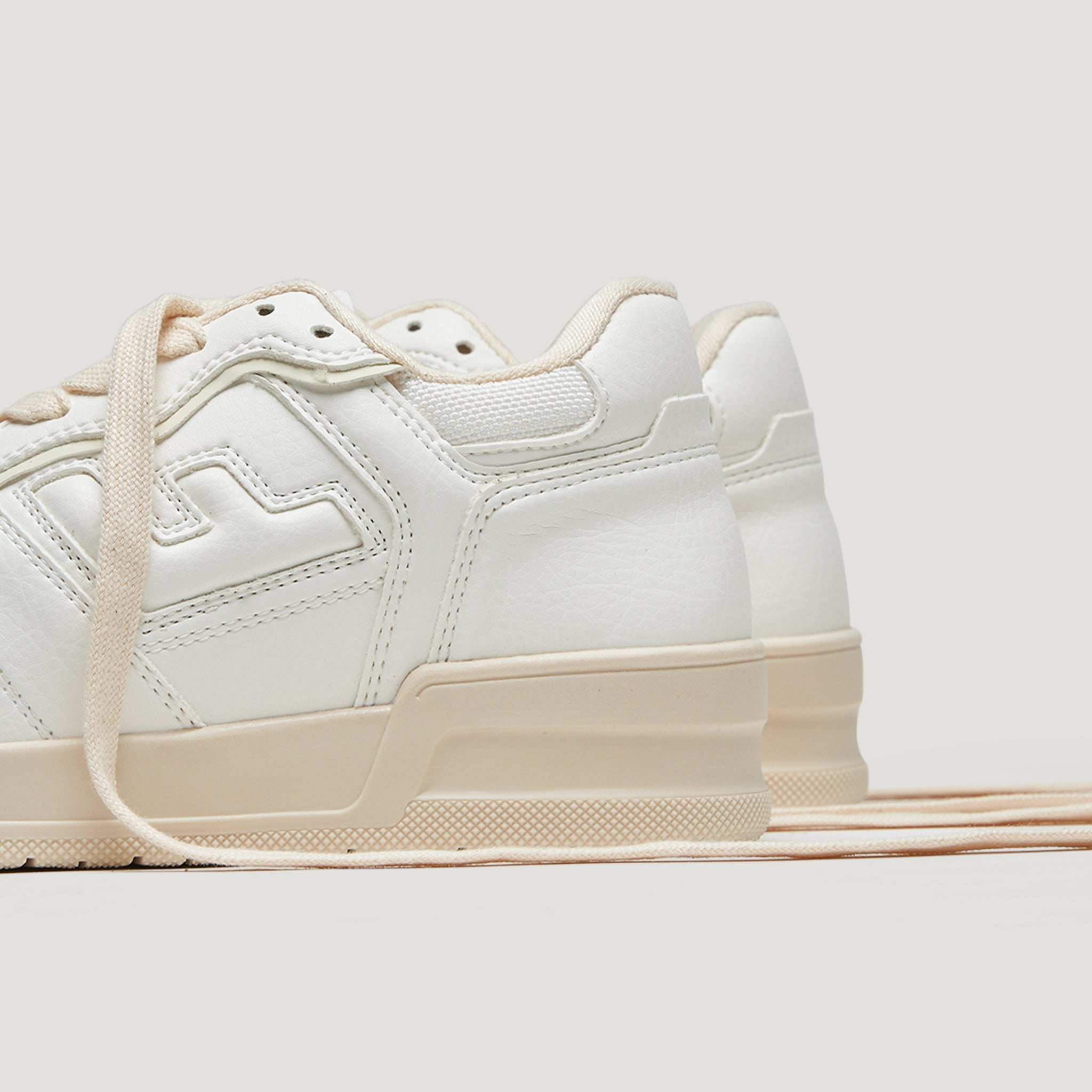 Weiße Sneakers mit beigefarbener Sohle und Schnürsenkeln, seitlich fotografiert vor grauem Hintergrund.