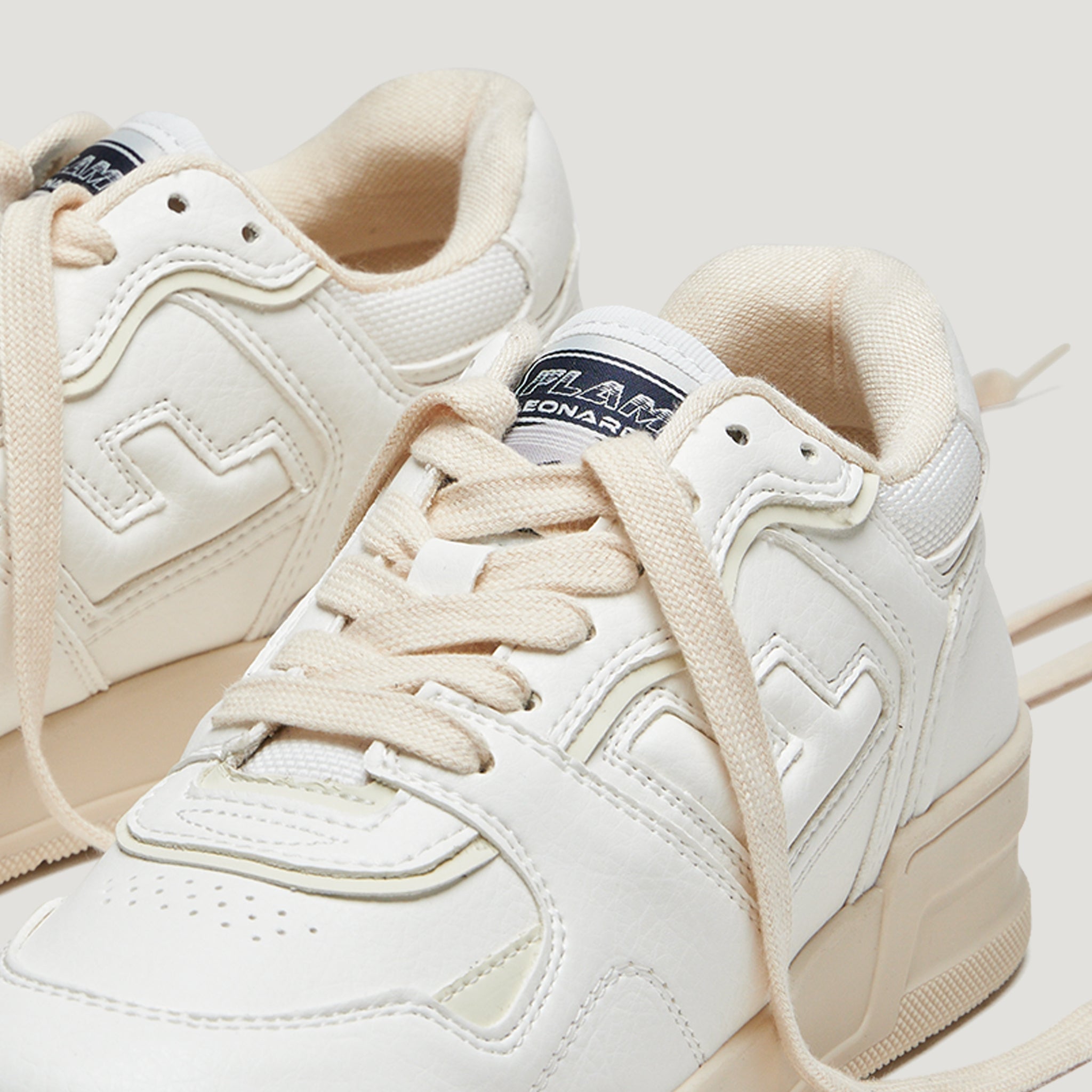 Nahaufnahme von weißen Sportschuhen mit cremefarbenen Schnürsenkeln auf hellgrauem Hintergrund.