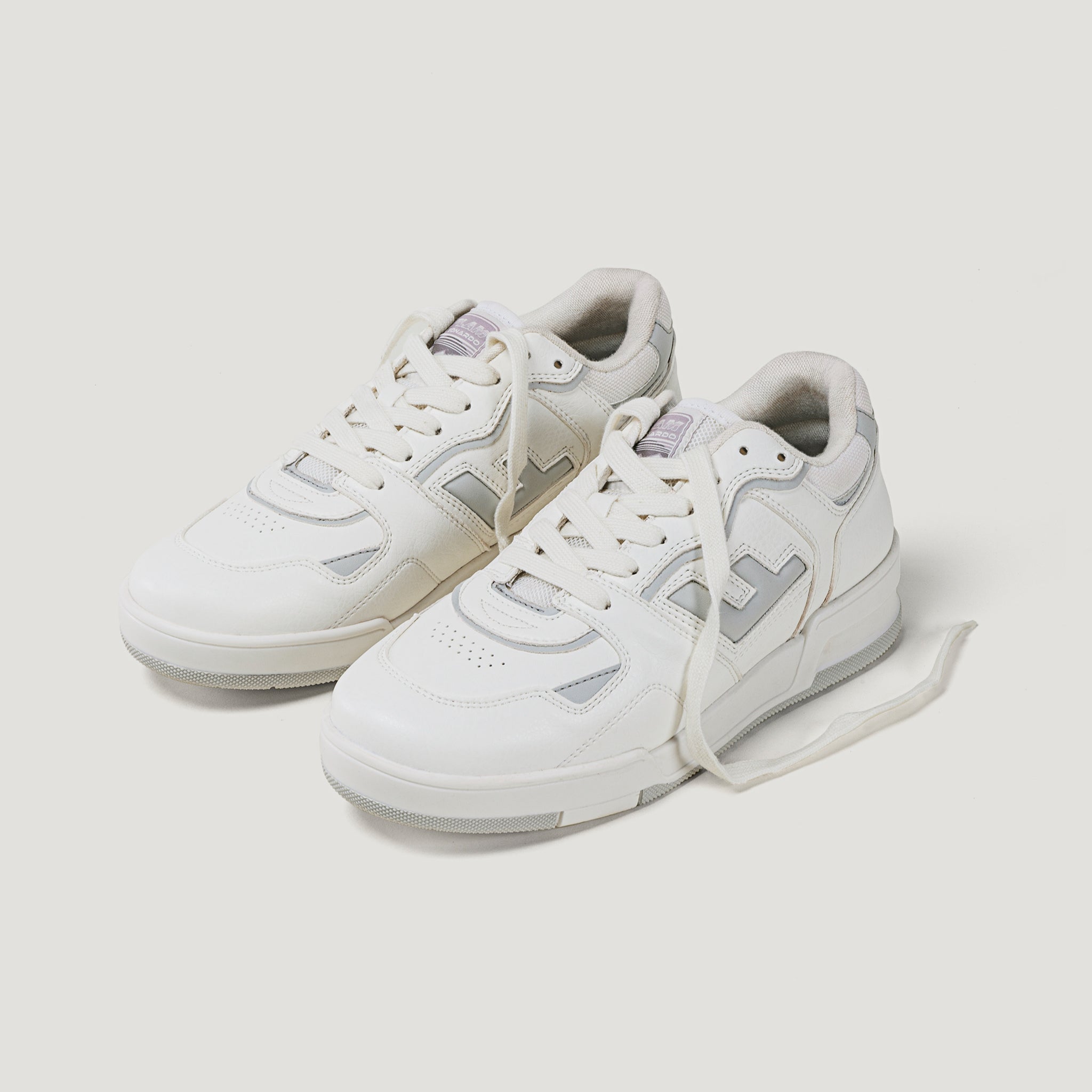 Weiße Turnschuhe mit grauen Akzenten und Schnürsenkeln, auf weißem Hintergrund.