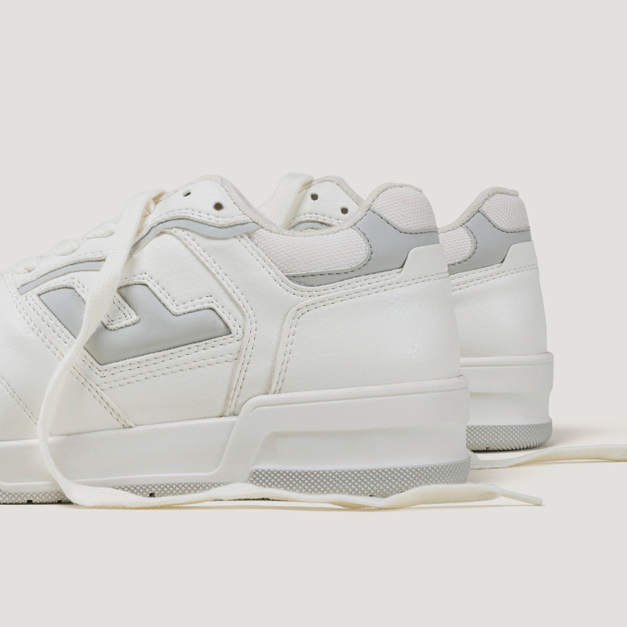 Weiße Sneaker mit grauen Details und langen Schnürsenkeln auf hellem Hintergrund, seitlich betrachtet.