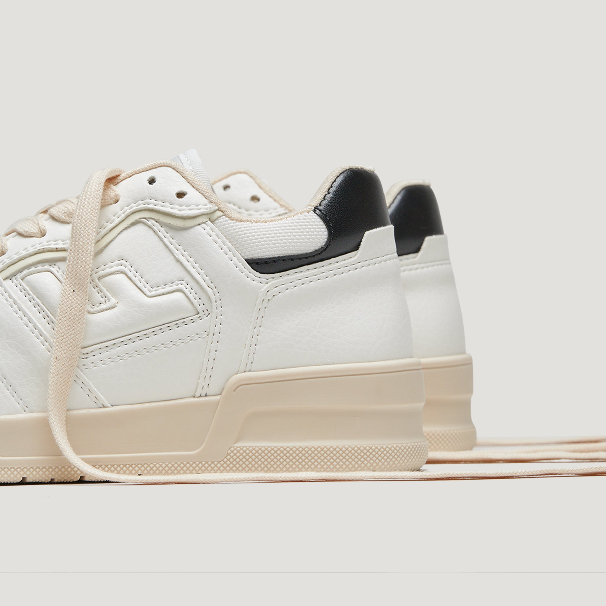 Nahaufnahme von weißen Sneakers mit beigen Sohlen und schwarzen Fersen, teilweise mit einem Schnürsenkel versehen.