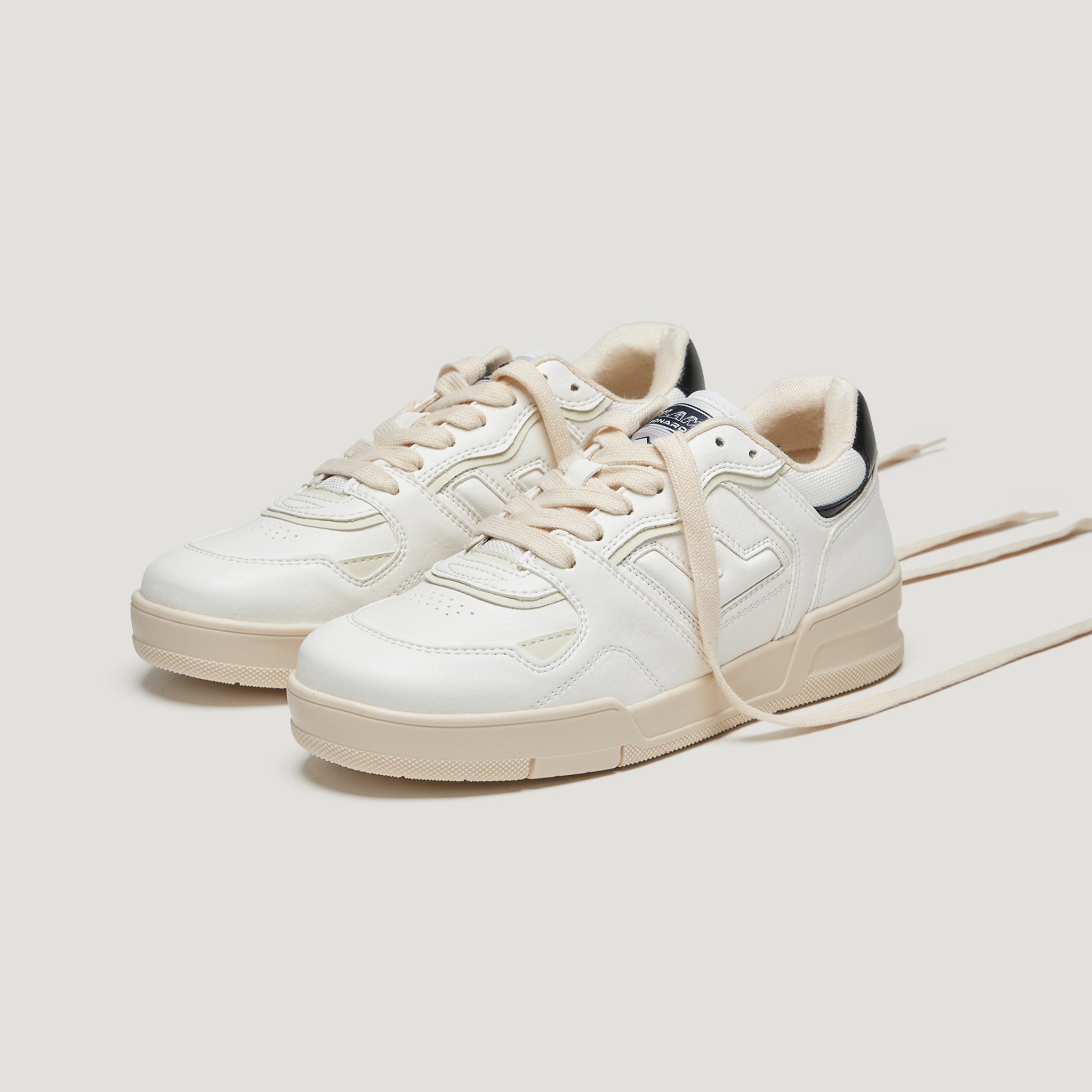 Weiße Sneaker mit beigen Details und Schnürsenkeln, vor weißem Hintergrund.