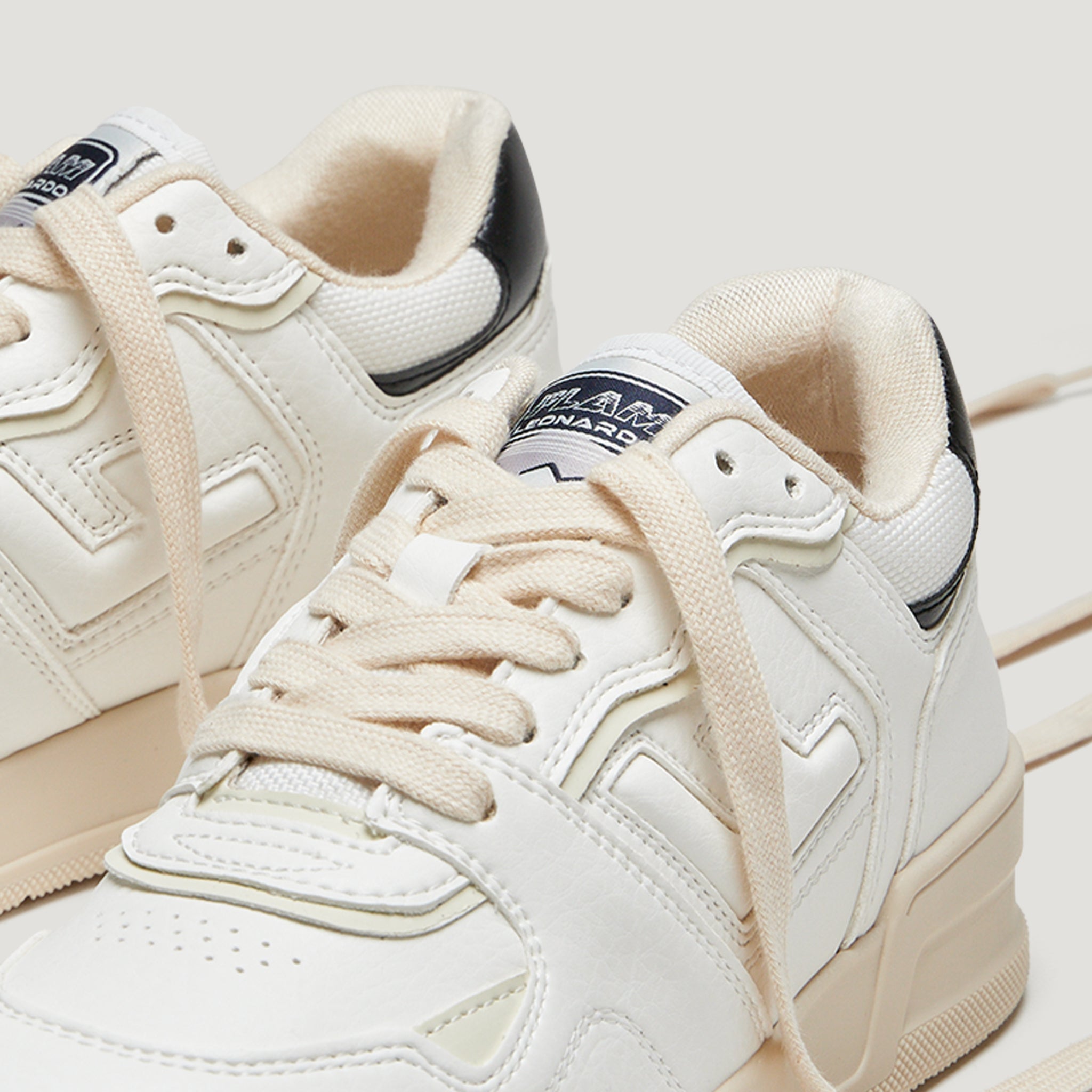 Weiße Turnschuhe mit cremefarbenen Schnürsenkeln und schwarzen Fersenakzenten auf hellem Hintergrund.