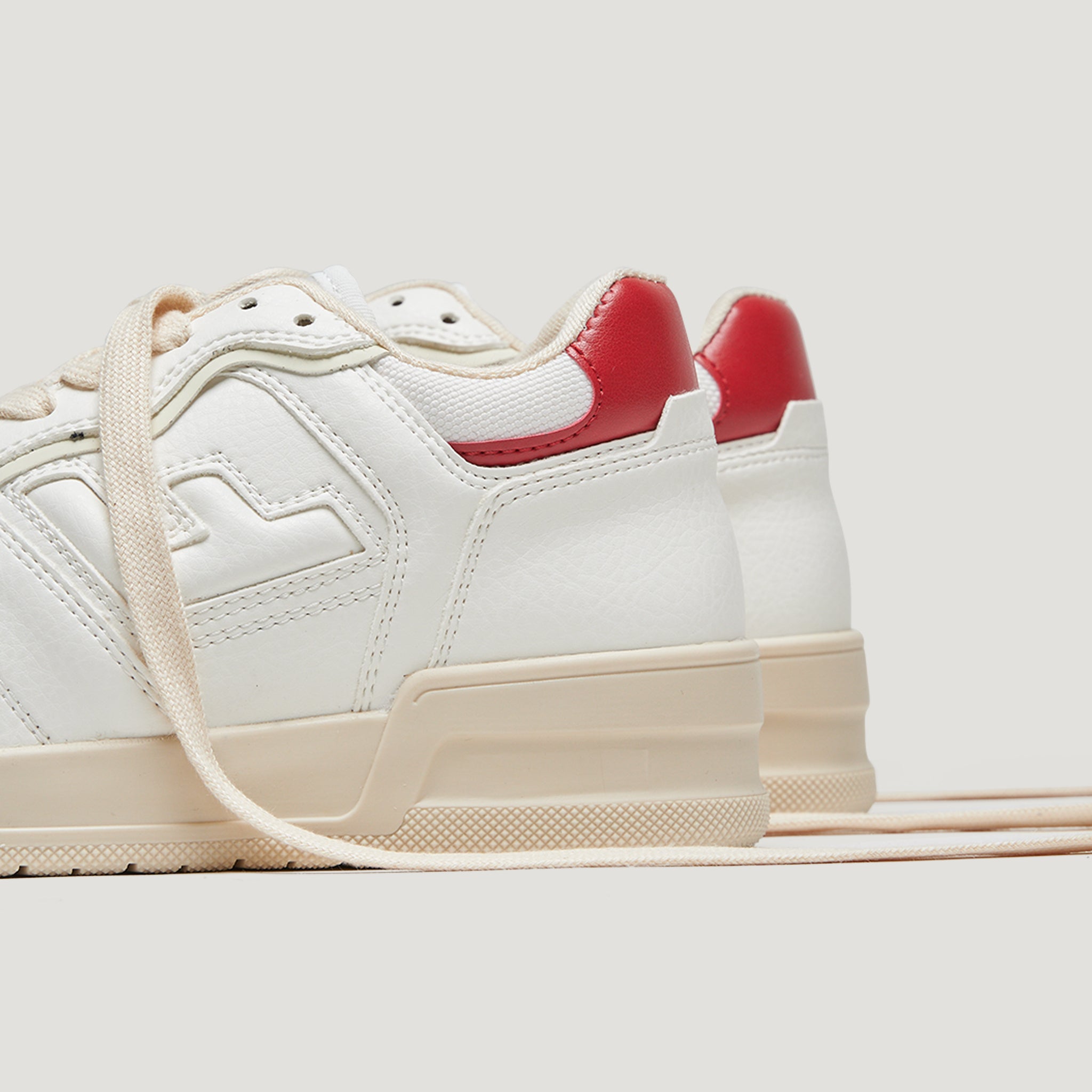 Weiße Turnschuhe mit cremefarbenen Schnürsenkeln und roten Fersenakzenten auf hellem Hintergrund.