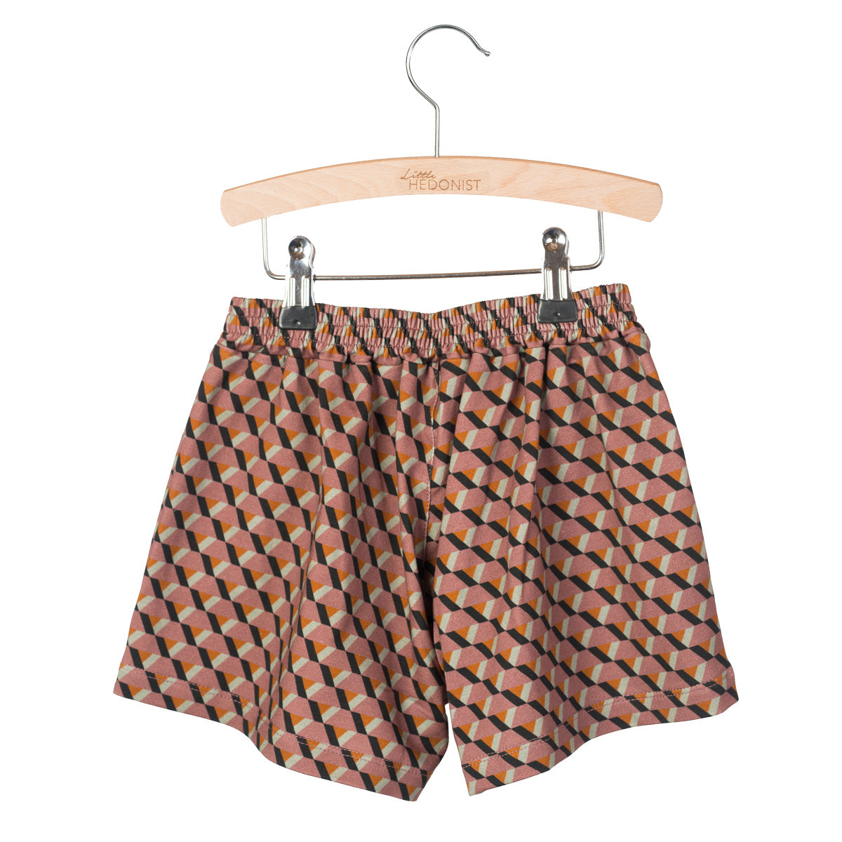 Ein Paar Kindershorts mit geometrischem Muster in Orange-, Schwarz- und Beigetönen, aufgehängt an einem Holzbügel mit dem eingravierten Logo Little HEDONIST.