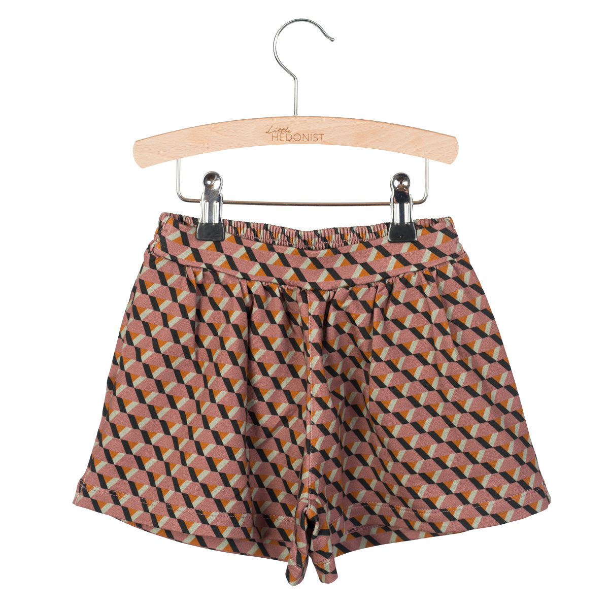 Ein Paar braune Shorts mit einem geometrischen Muster in Schwarz, Gelb und Rosa, die auf einem Holzbügel mit Metallklammern befestigt sind.