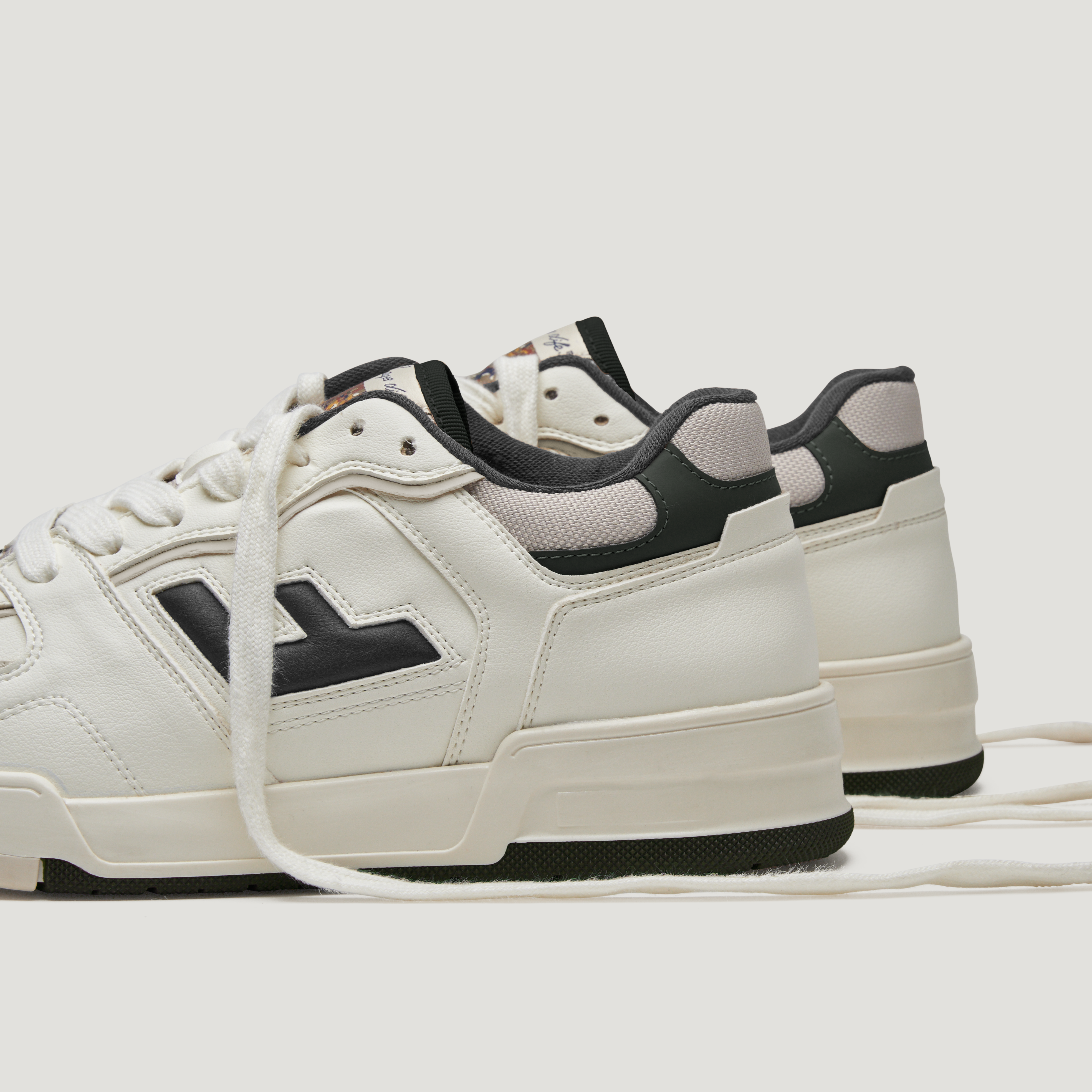 Weiße Sneaker mit schwarzen Details und Schnürsenkeln auf weißem Hintergrund.