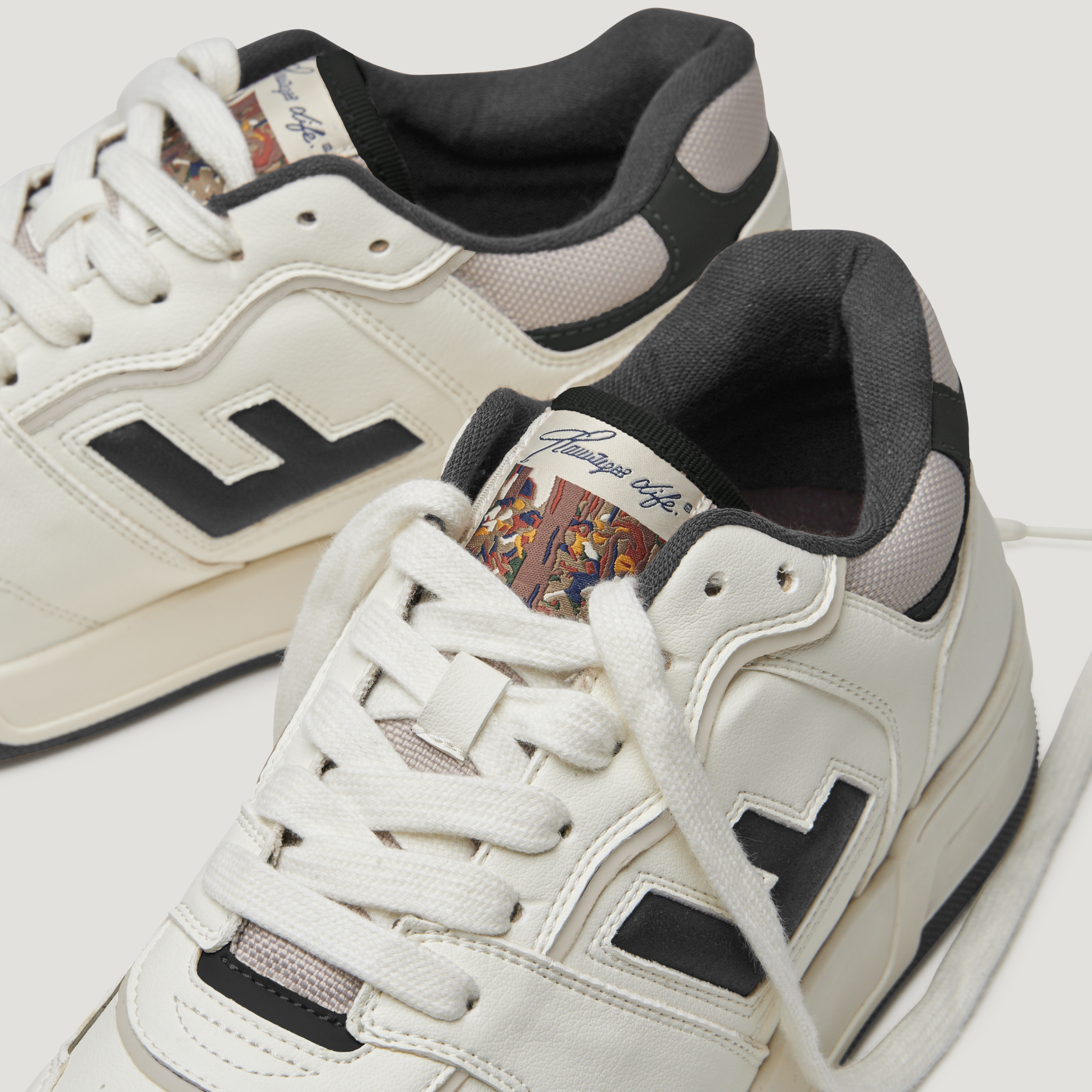 Weiße Turnschuhe mit schwarzem Logo und bunter Zunge, darauf ein Muster aus klassischen Kunstwerken.