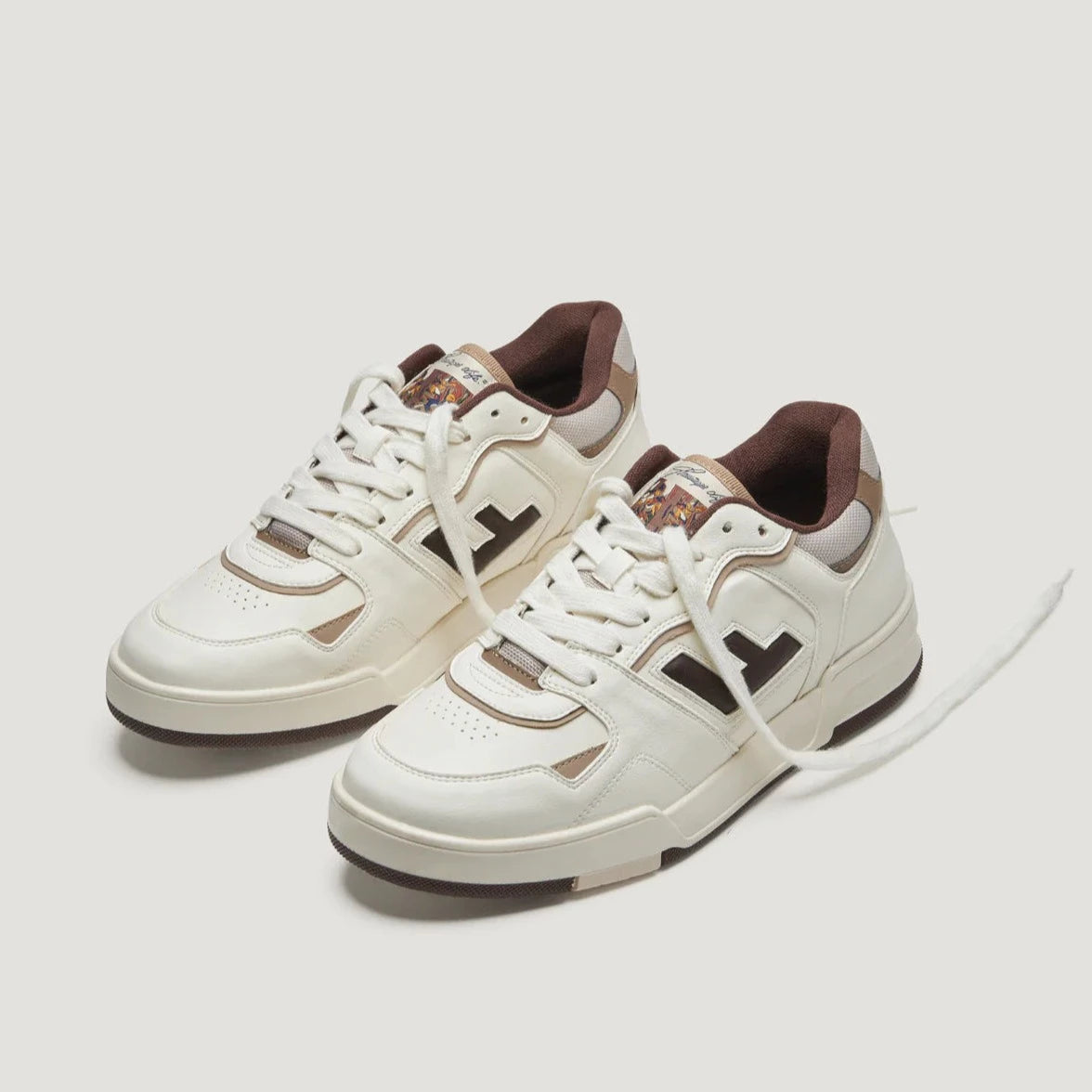 Weiße Turnschuhe mit braunen Details und einem dunklen Gummisohle auf hellem Hintergrund.