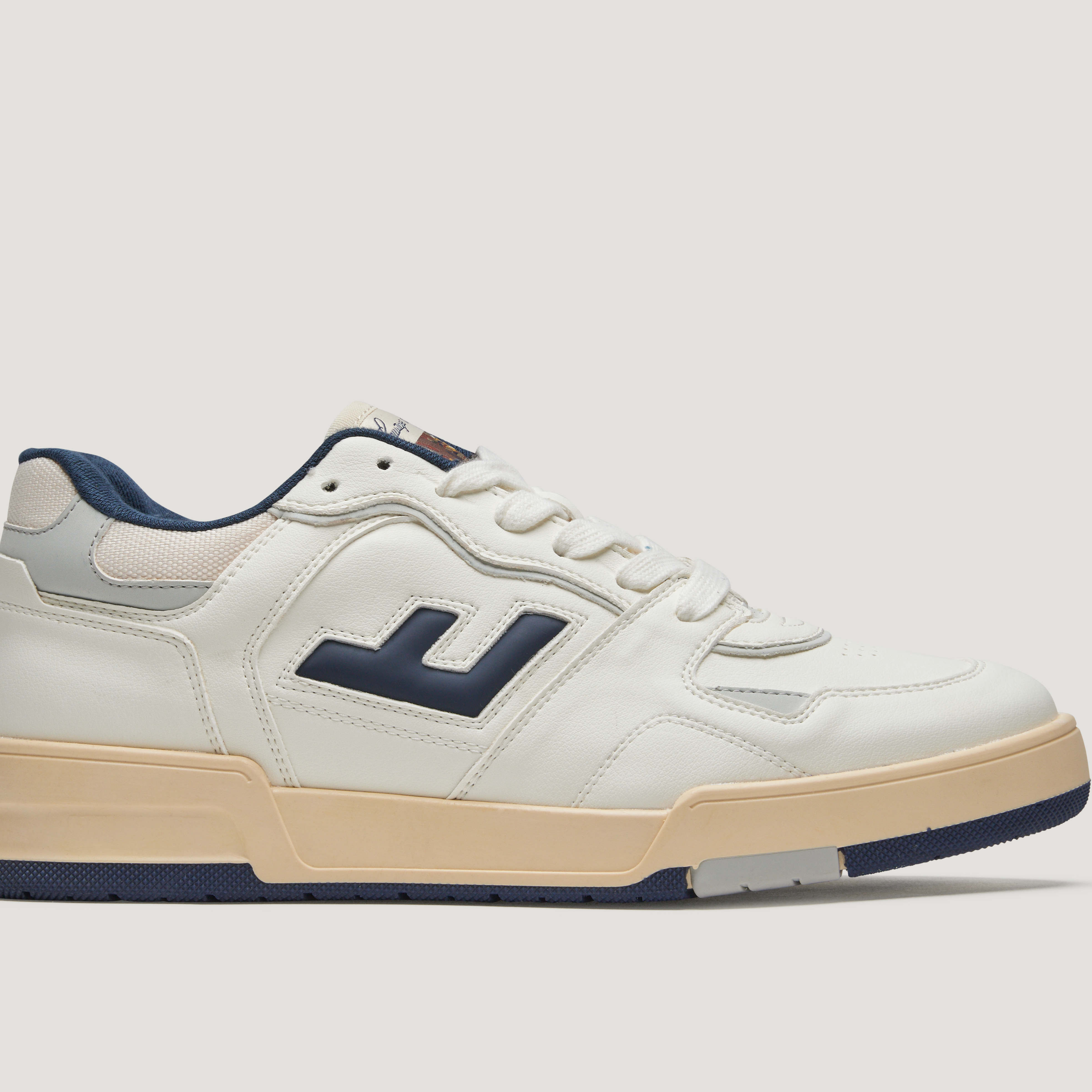 Weißer Sneaker mit marineblauem Logo, blauer Ferse und cremefarbener Sohle auf weißem Hintergrund.