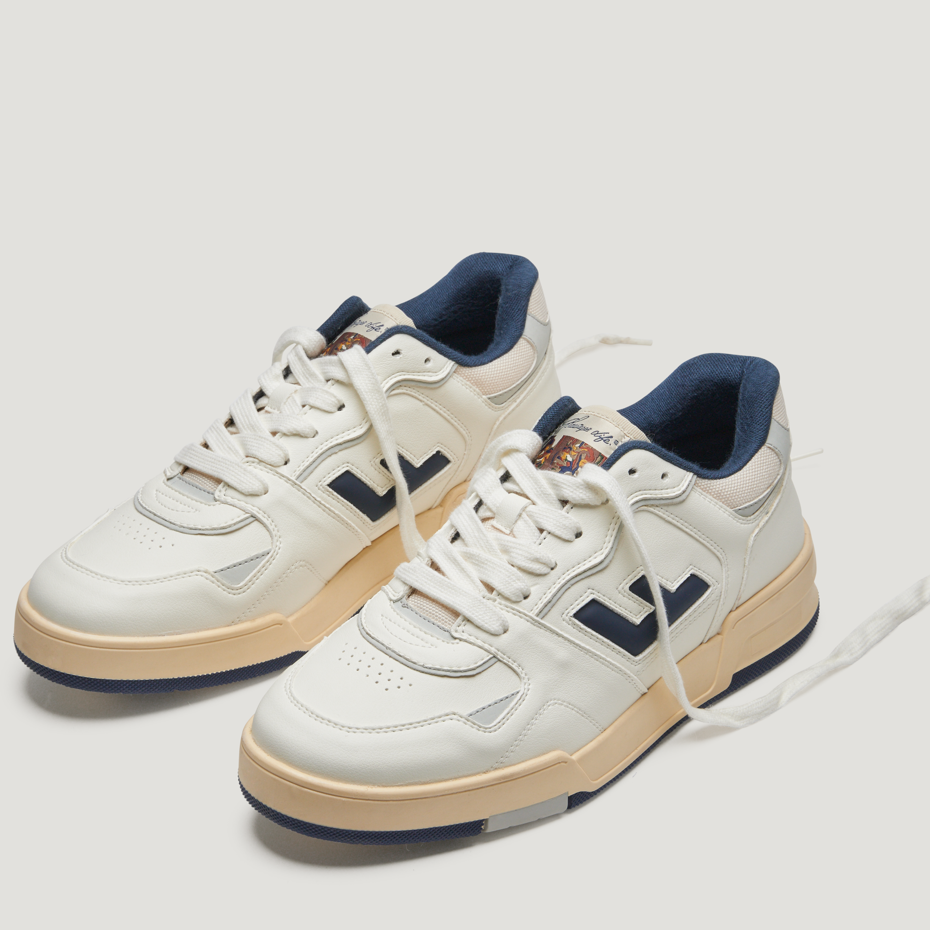 Weiße Sneaker mit blauen Akzenten und beigefarbener Sohle, mit geschnürten weißen Schnürsenkeln, auf hellem Hintergrund.