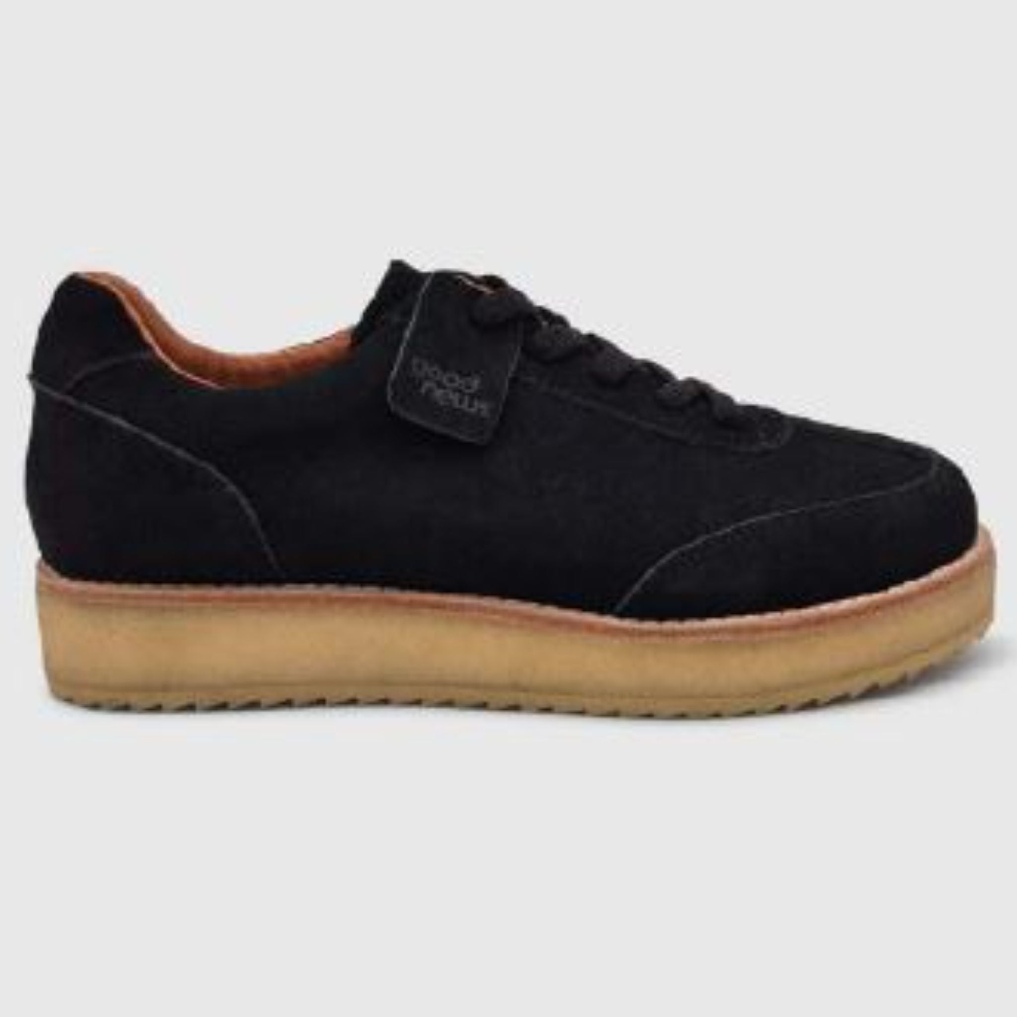Ein schwarzer Wildleder-Sneaker mit hellbrauner Gummisohle und schwarzen Schnürsenkeln, dargestellt in einer seitlichen Profilansicht vor einem schlichten hellgrauen Hintergrund.