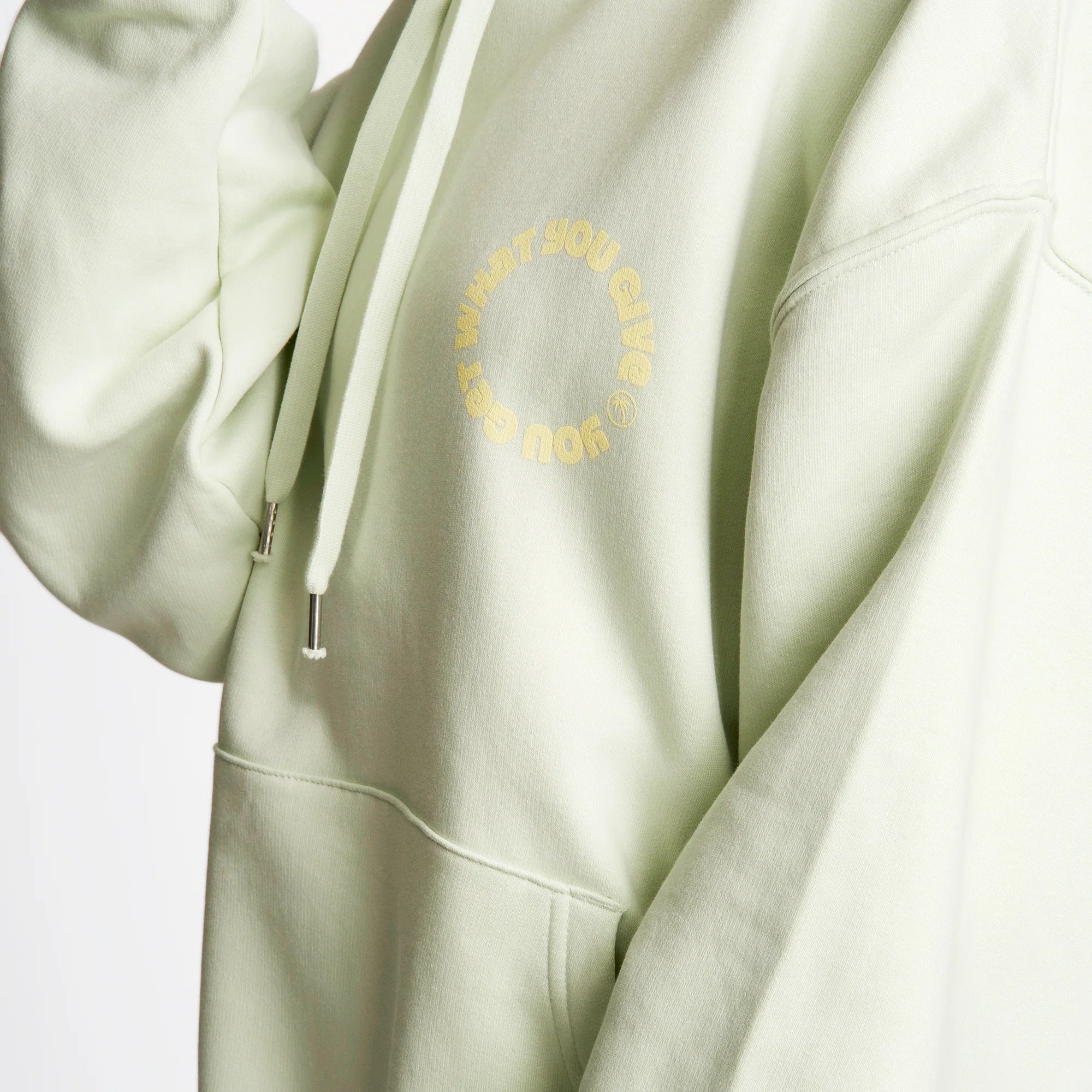 Hellgrüner Hoodie mit gelber, kreisförmiger Aufschrift auf der Brust und Sicht auf die Kapuze mit Kordelzügen.