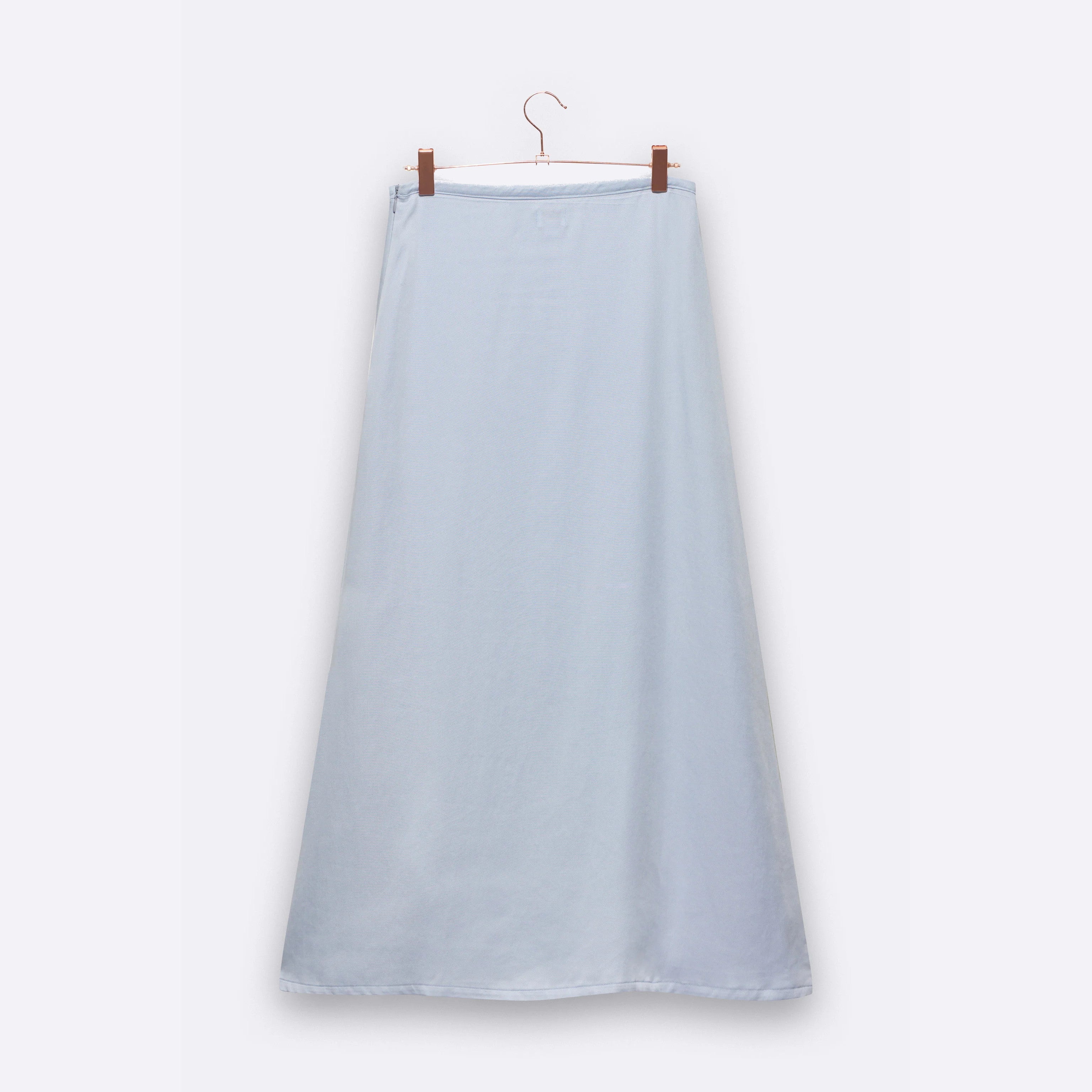 Ein langer, hellblauer Rock hängt an einem Kleiderbügel vor einem weißen Hintergrund.