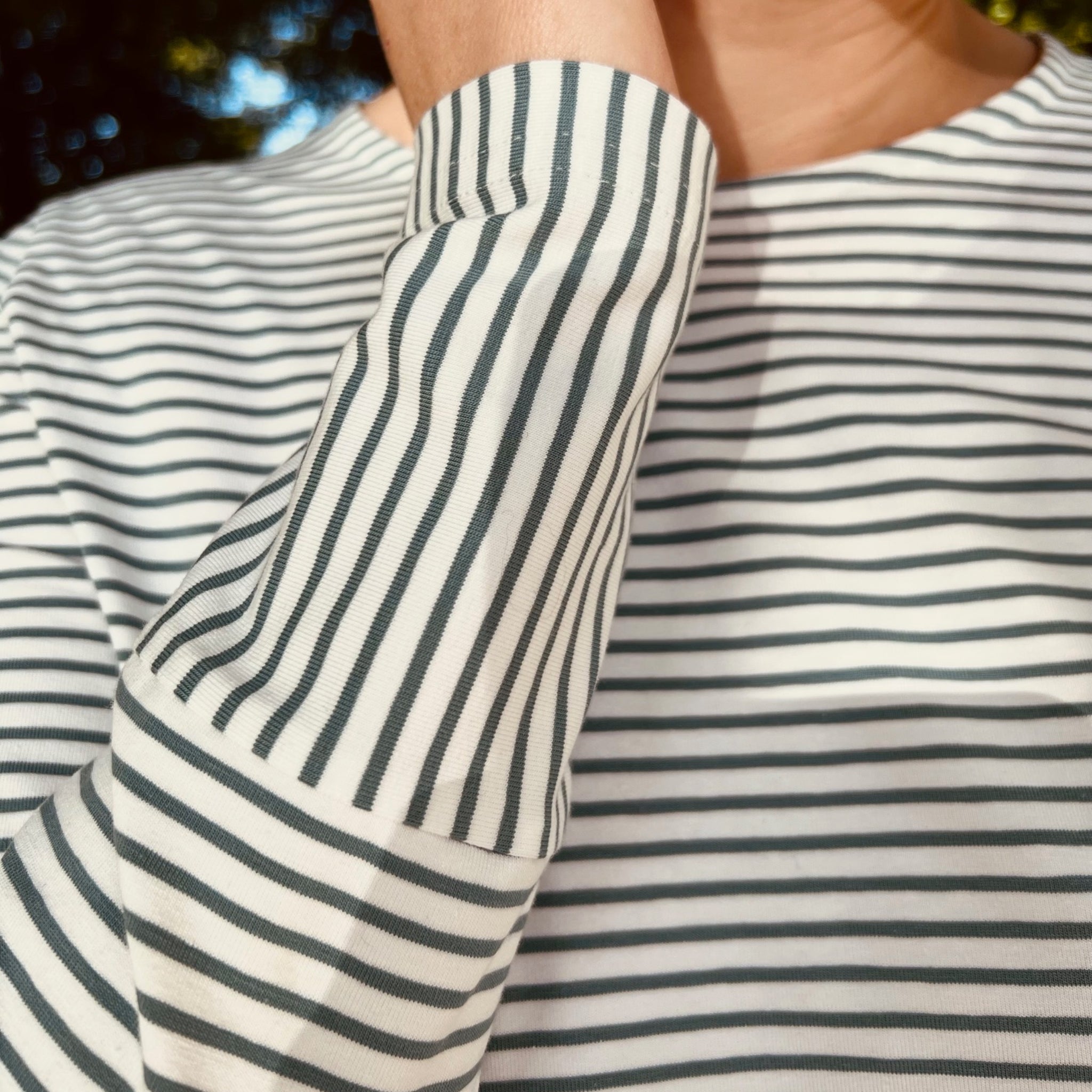 Person in einem gestreiften Langarm-Shirt hält den Arm nahe am Gesicht.