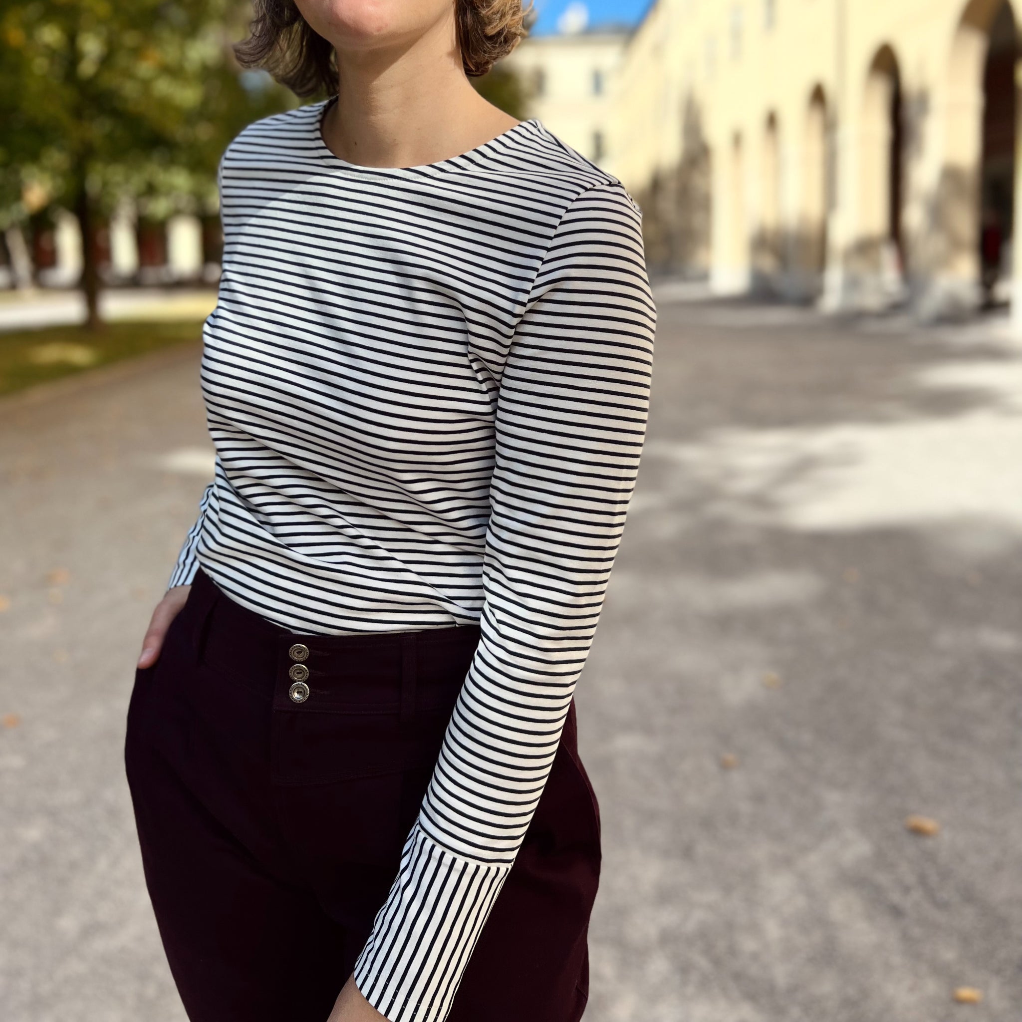 Eine Person mit einem gestreiften Oberteil steht draußen auf einem Gehweg neben einem Gebäude.