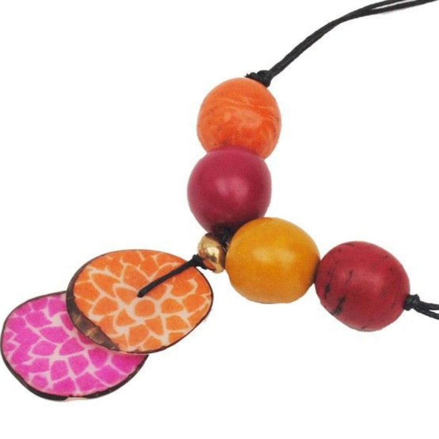 Eine farbenfrohe Halskette mit großen, runden Perlen in Orange, Gelb und Rot sowie zwei flachen, ovalen Anhängern in Orange und Rosa mit weißen Blumenmustern, aufgereiht auf einer schwarzen Schnur.