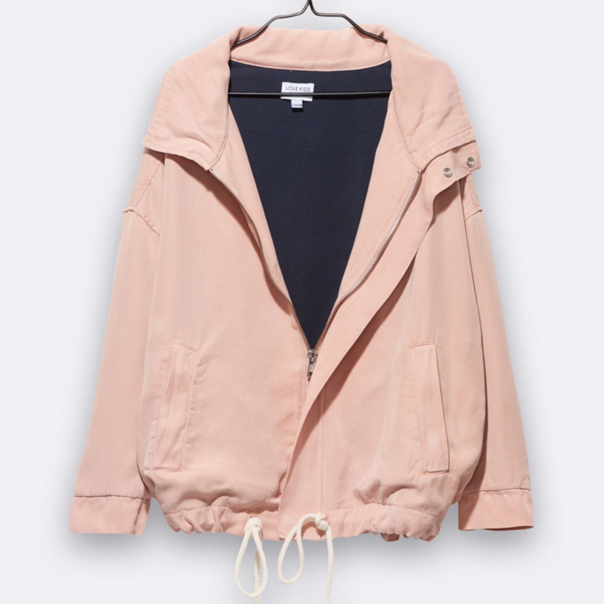 Eine hellrosa Jacke mit Reißverschluss, Kragen, Seitentaschen, Kordelzug am Saum und Druckknöpfen am Kragen, die auf einem Bügel vor einem unifarbenen Hintergrund präsentiert wird.