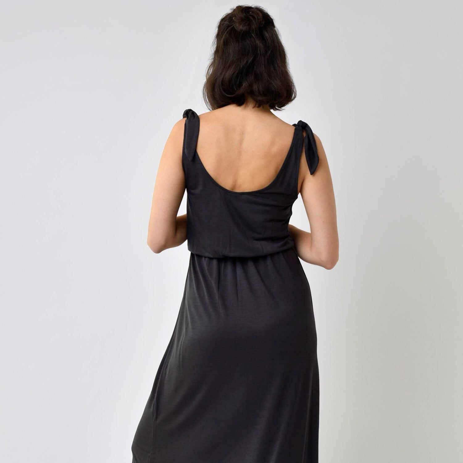 Frau in einem schwarzen Kleid mit tiefem Rückenausschnitt, von hinten gesehen, vor einem hellgrauen Hintergrund.