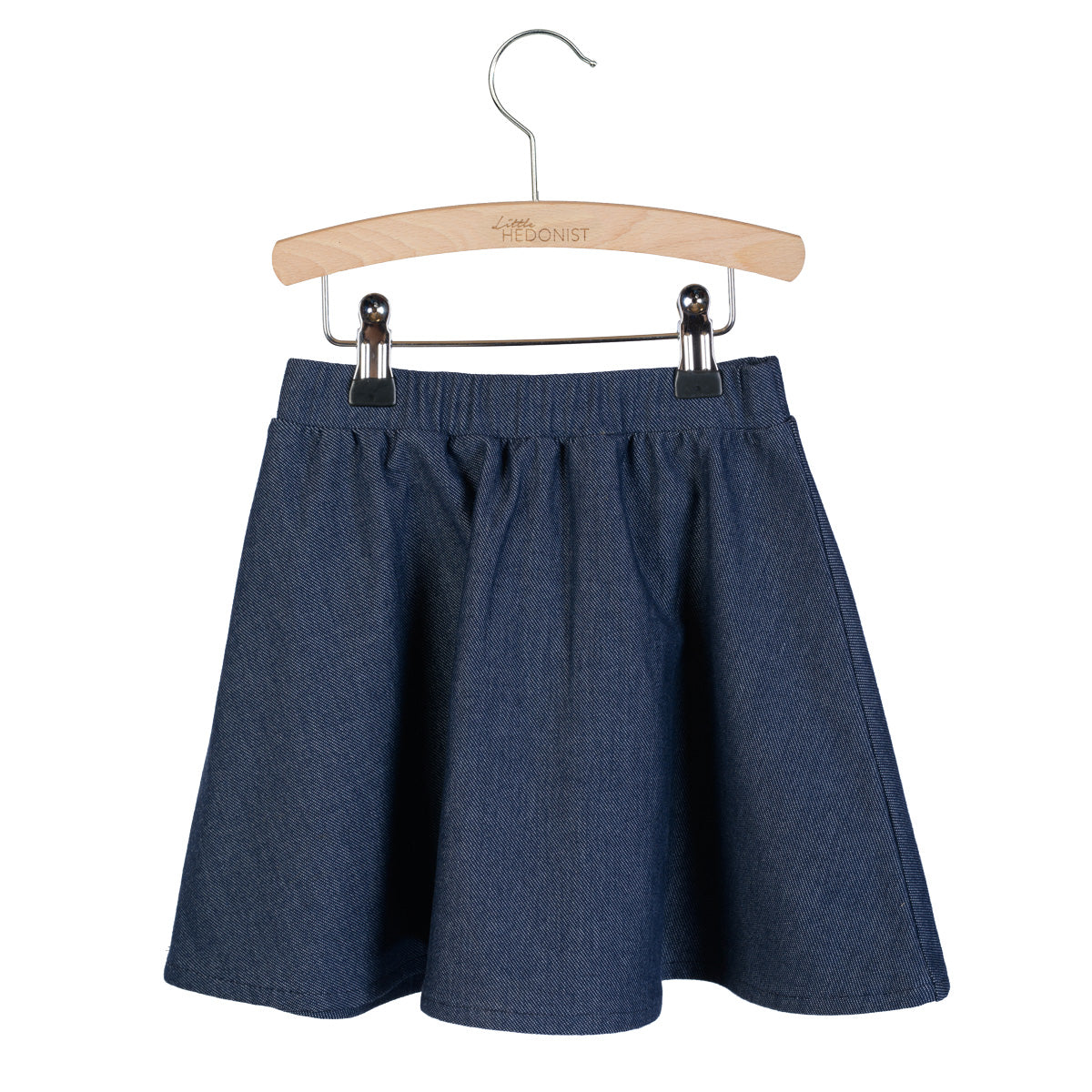 Ein blauer Jeansrock mit elastischem Bund, ausgestellt auf einem Holzbügel mit Metallklammern vor einem weißen Hintergrund.