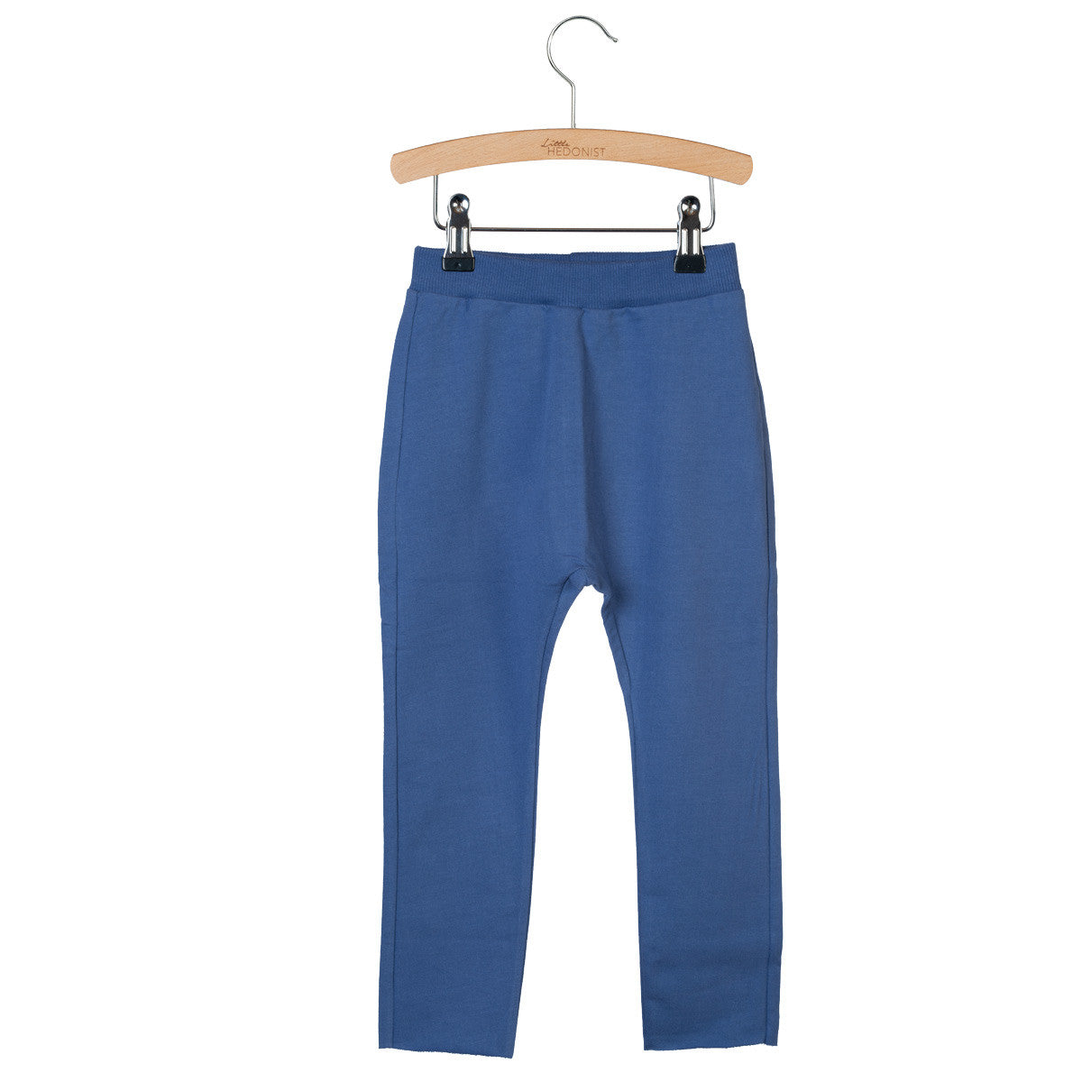 Eine blaue Kinderhose hängt an einem Holzbügel mit schwarzen Klammern vor einem schlichten weißen Hintergrund.