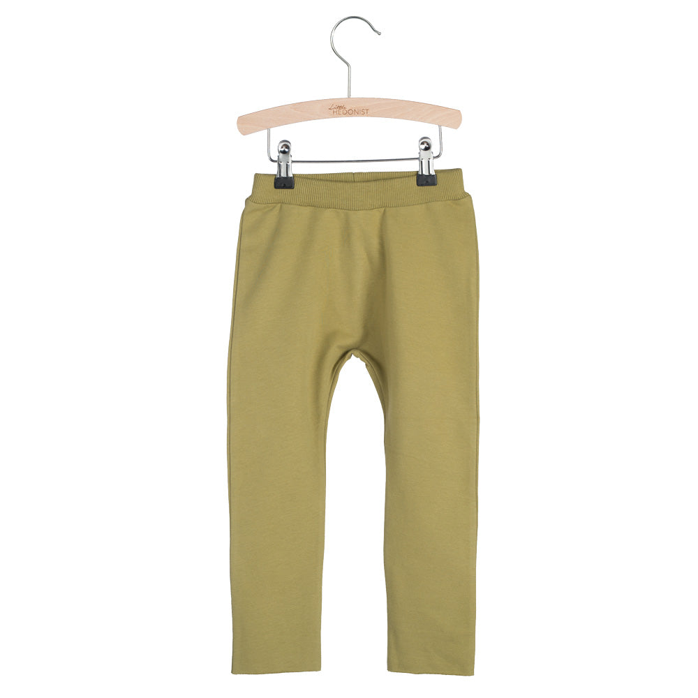 Ein Paar olivgrüne Kinderleggings, die auf einem Holzbügel vor einem weißen Hintergrund hängen.