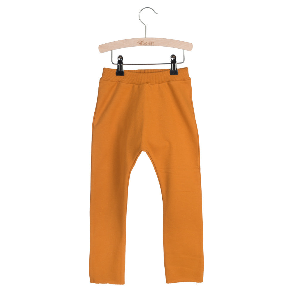 Ein Paar senfgelbe Kinderleggins hängt auf einem Holzbügel vor weißem Hintergrund.