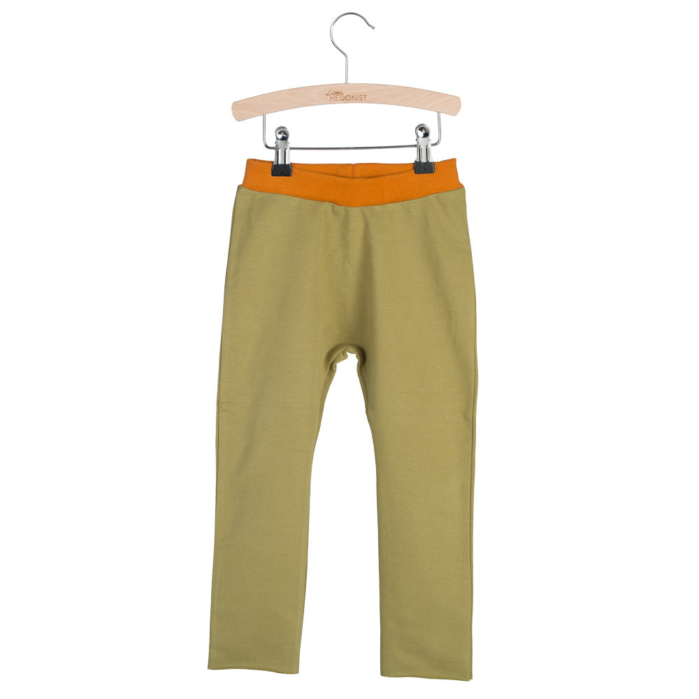 Olivgrüne Kinderleggings mit orangefarbenem Bund, aufgehängt an einem Holzbügel vor weißem Hintergrund.