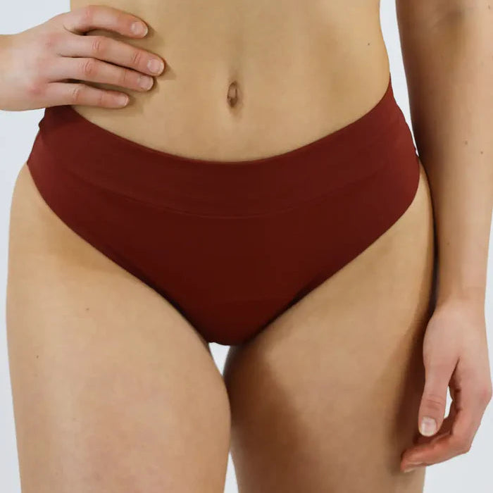 Person trägt einen burgunderroten Bikiniunterteil vor neutralem Hintergrund.