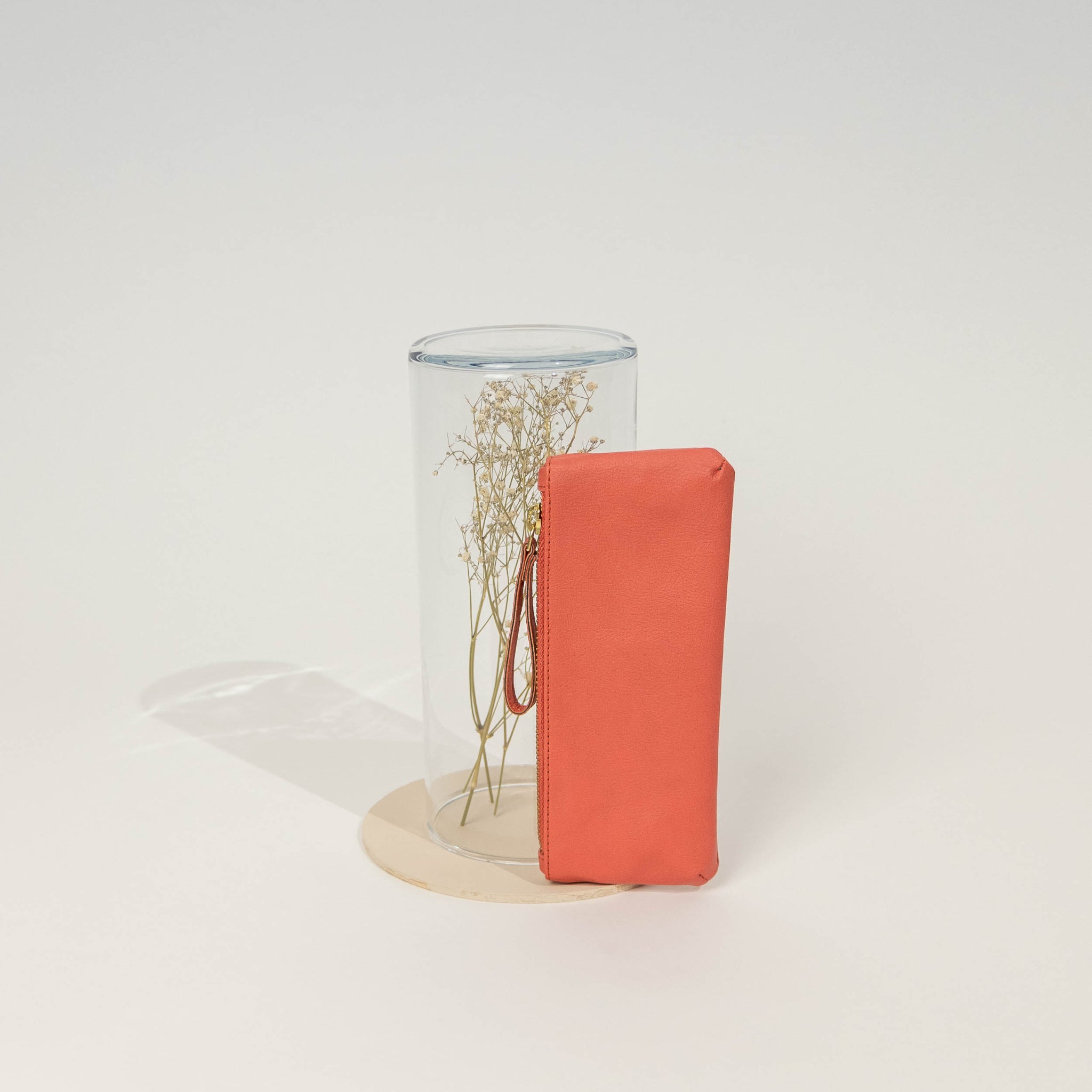 Rotes Etui und durchsichtige Vase mit getrockneten Zweigen auf heller Oberfläche.