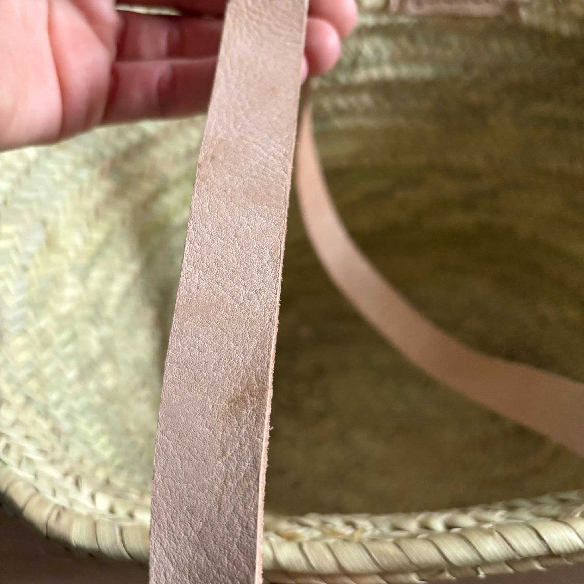 Nahaufnahme eines Riemens aus Leder, der an einem gewebten Korb befestigt ist, mit einer Hand im Hintergrund, die ihn hält.