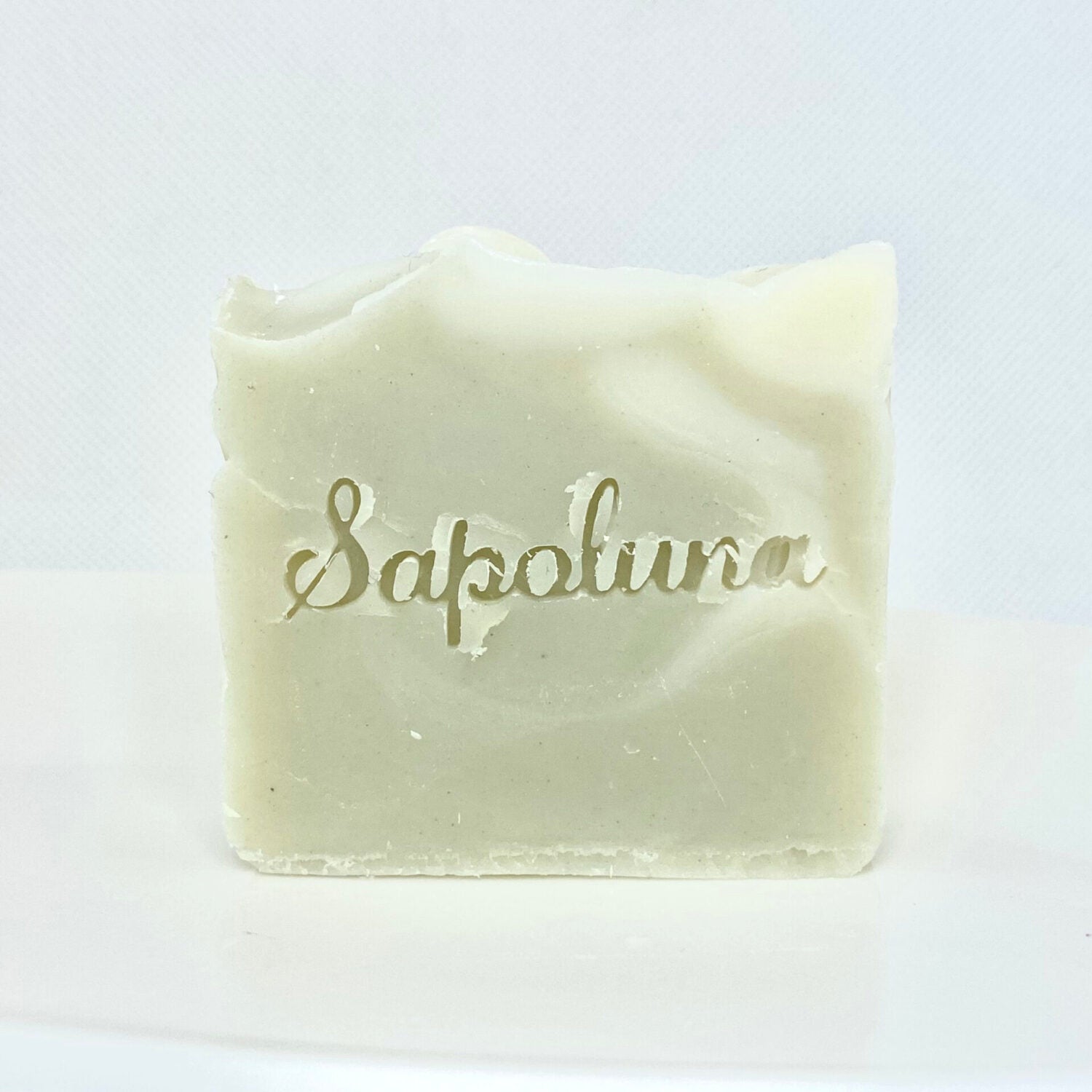 Ein beiger Seifenblock mit dem eingravierten Schriftzug "Sapolina" auf weißem Hintergrund.