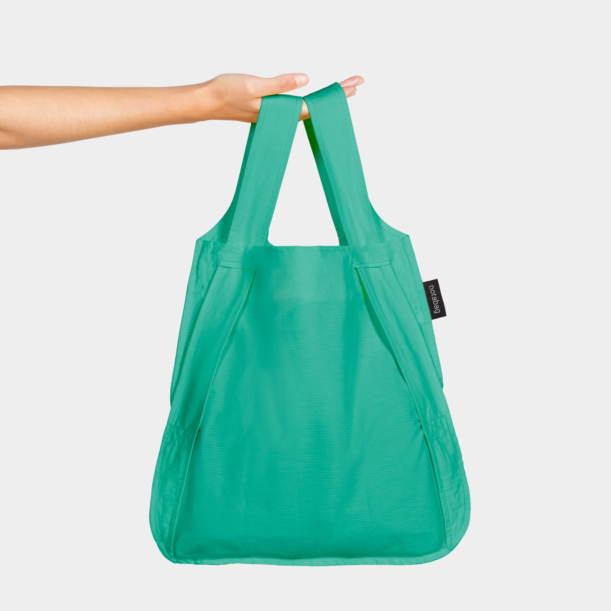 Eine grüne Stofftasche wird von einer Hand vor einem weißen Hintergrund gehalten.