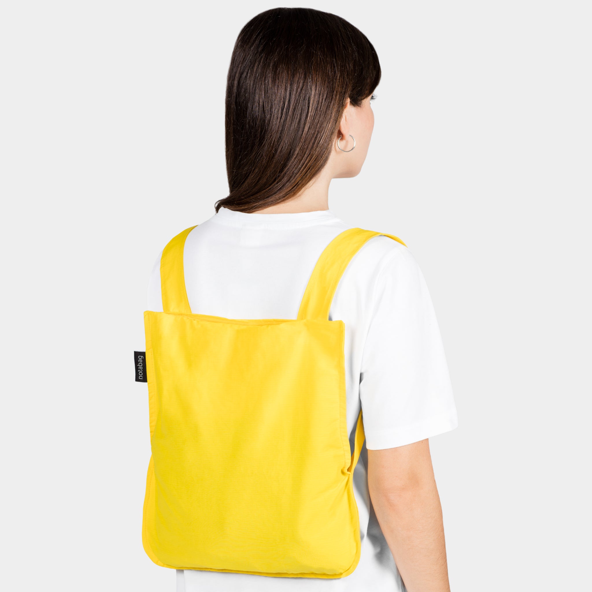Person mit gelbem Rucksack und weißem Shirt, Rückenansicht.