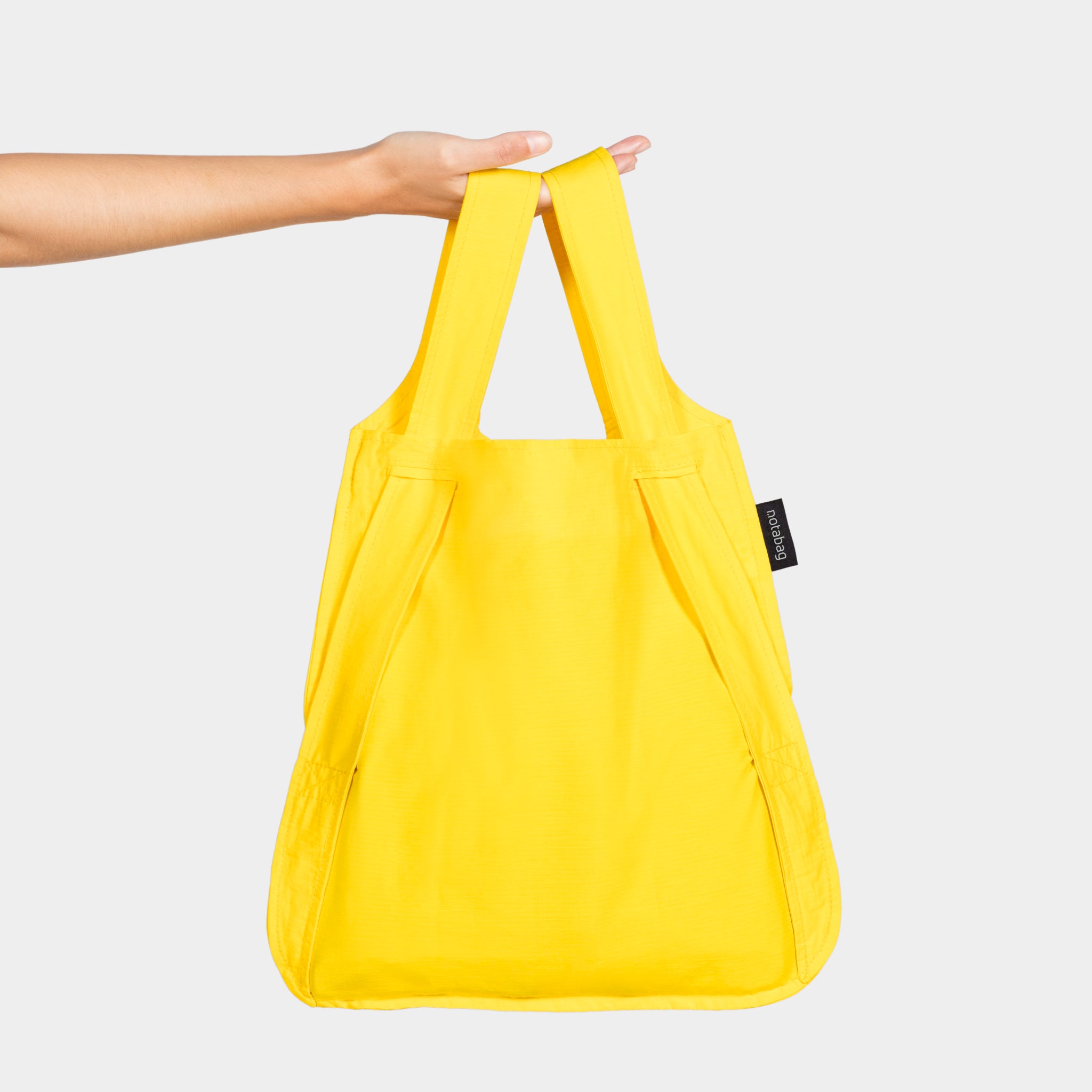 Eine Hand hält eine leuchtend gelbe Stofftasche mit zwei Tragegriffen vor einem weißen Hintergrund.
