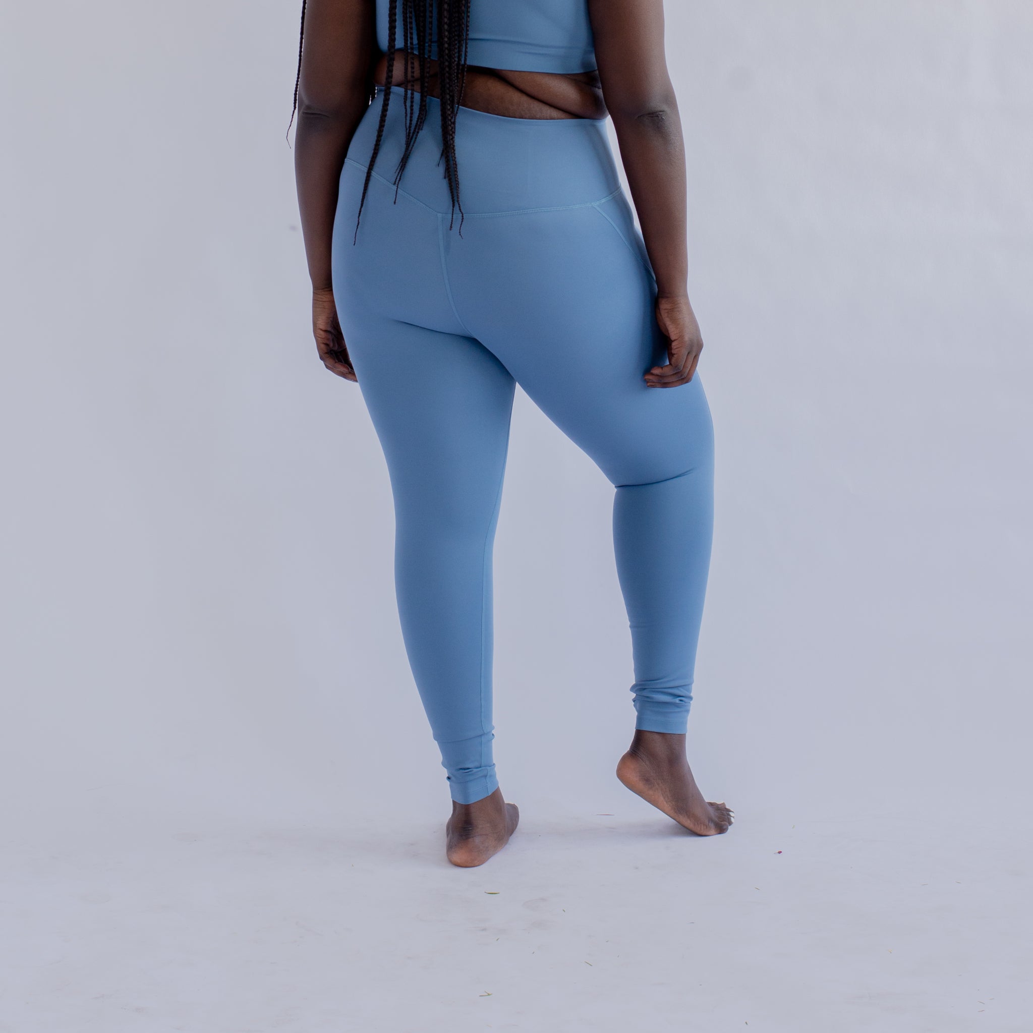 Person in blue Sportkleidung von hinten, barfuß auf hellem Hintergrund stehend.