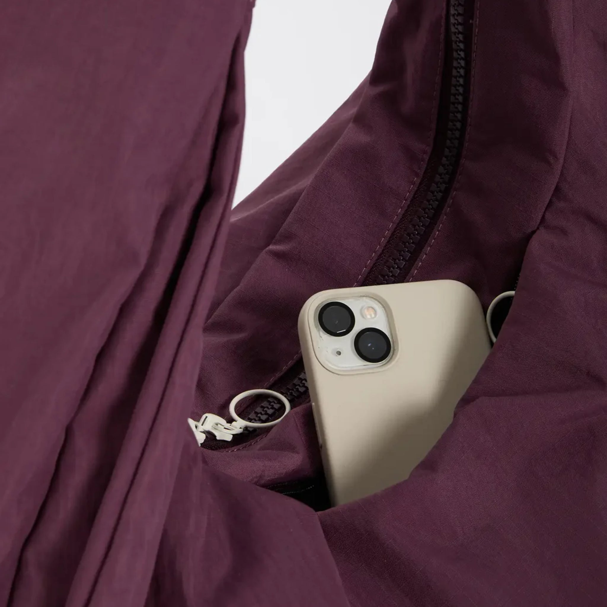 Ein cremefarbenes Smartphone, das teilweise in einer Reißverschlusstasche eines lilafarbenen Kleidungsstücks oder einer Tasche steckt.