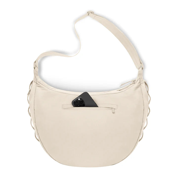 Eine cremefarbene Umhängetasche mit geschwungener Form und einem teilweise geöffneten Reißverschlussfach auf der Vorderseite, in dem sich ein schwarzes Smartphone befindet. Die Tasche hat einen langen verstellbaren Riemen und geflochtene Seitenteile.