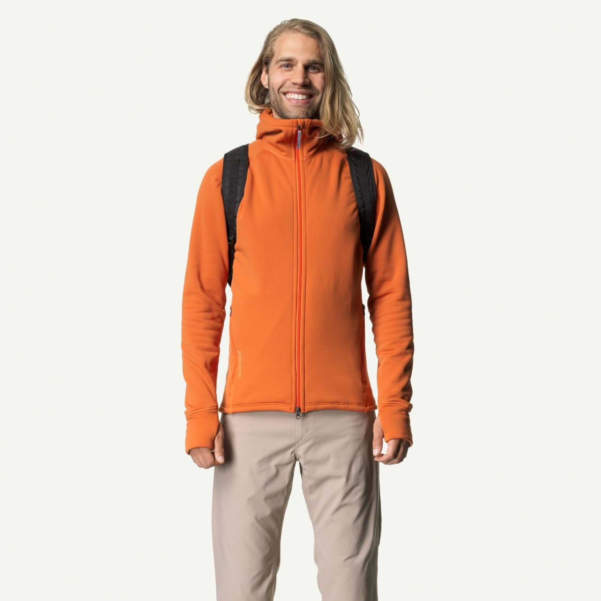Ein Mann mit langen Haaren trägt einen orangefarbenen Hoodie und einen schwarzen Rucksack vor einem weißen Hintergrund.