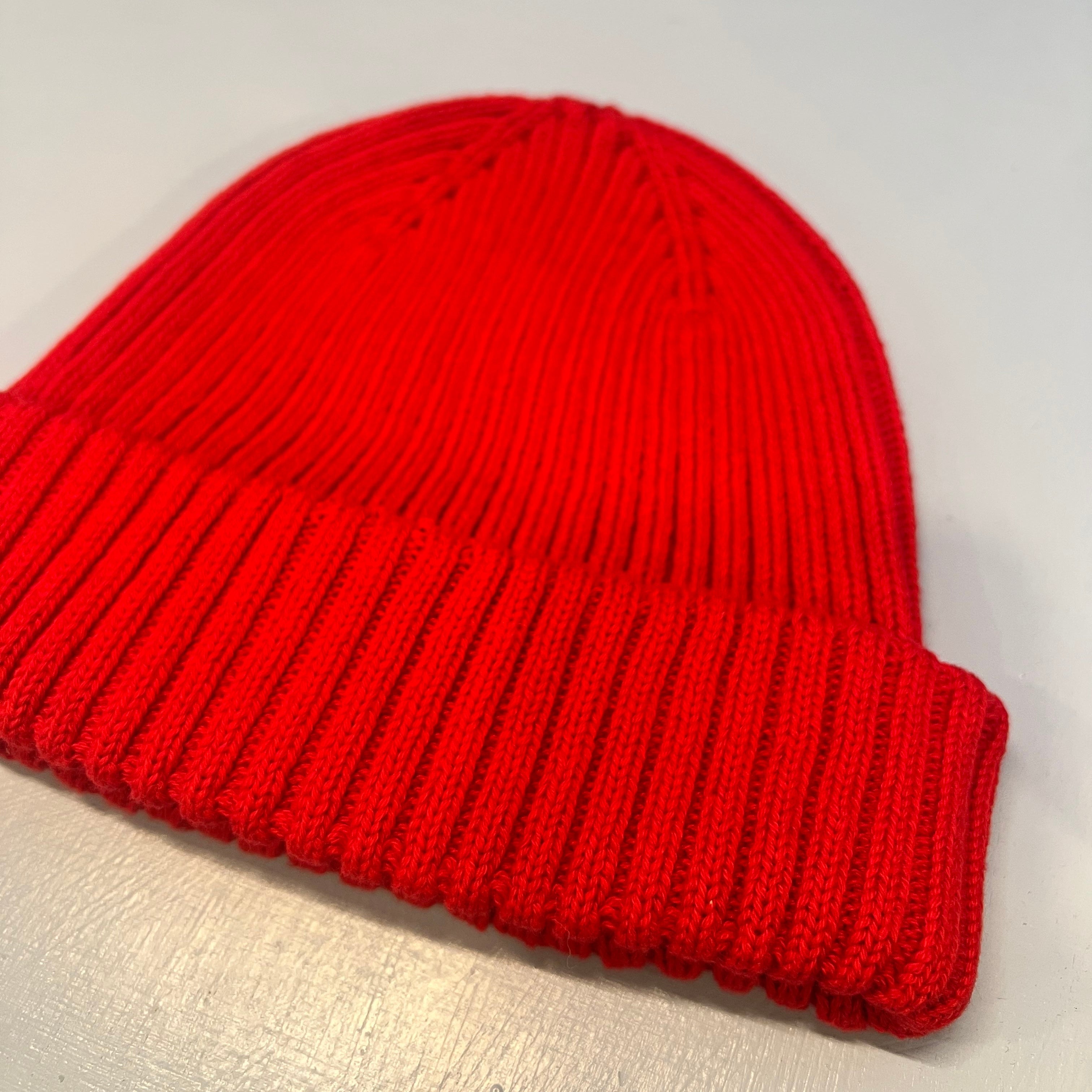 Eine leuchtend rote Strickmütze mit umgeschlagener Krempe liegt flach auf einer hellen Fläche.